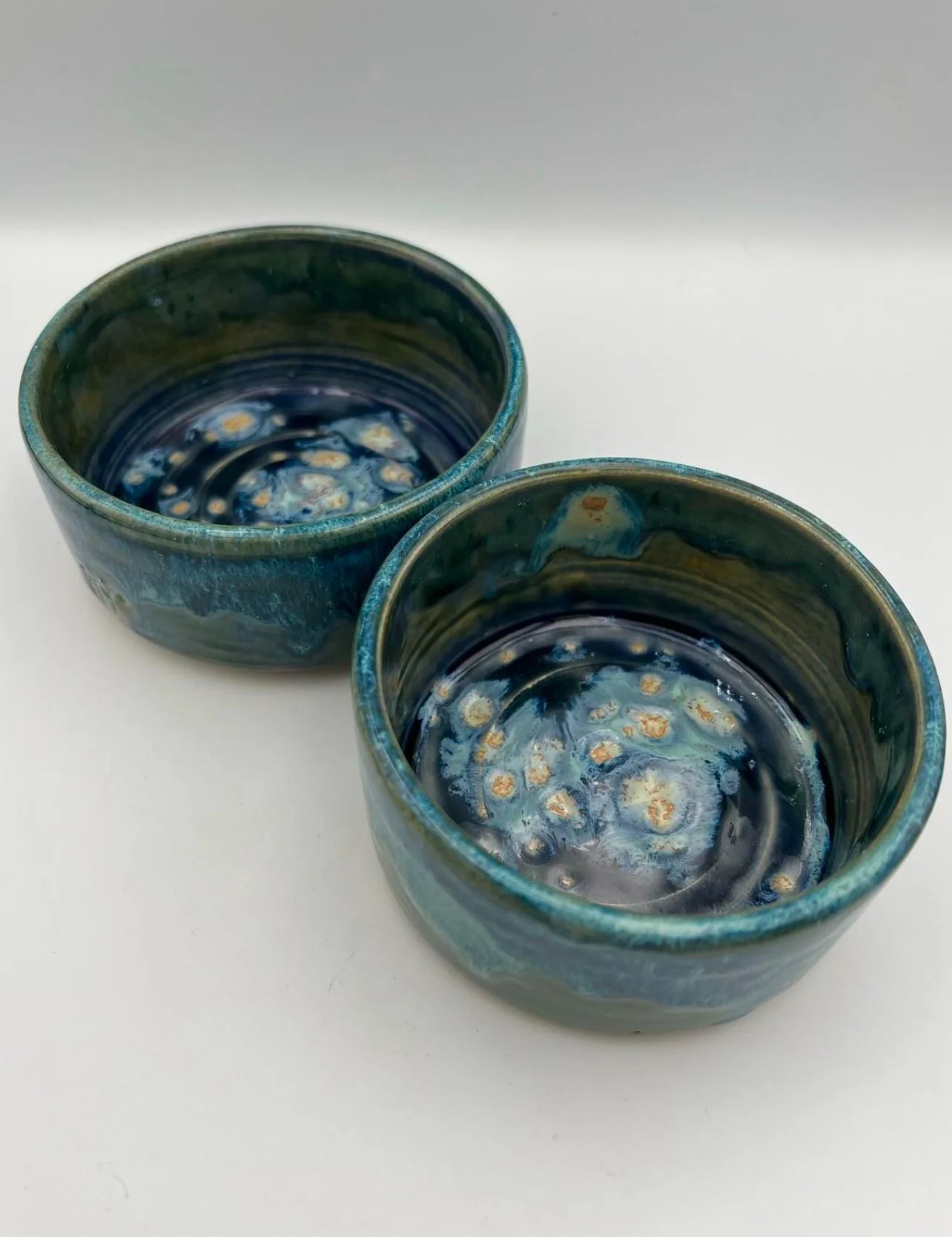 Twee handgemaakte keramieken kommen met blauwe en groene glazuur, geplaatst op een witte ondergrond.