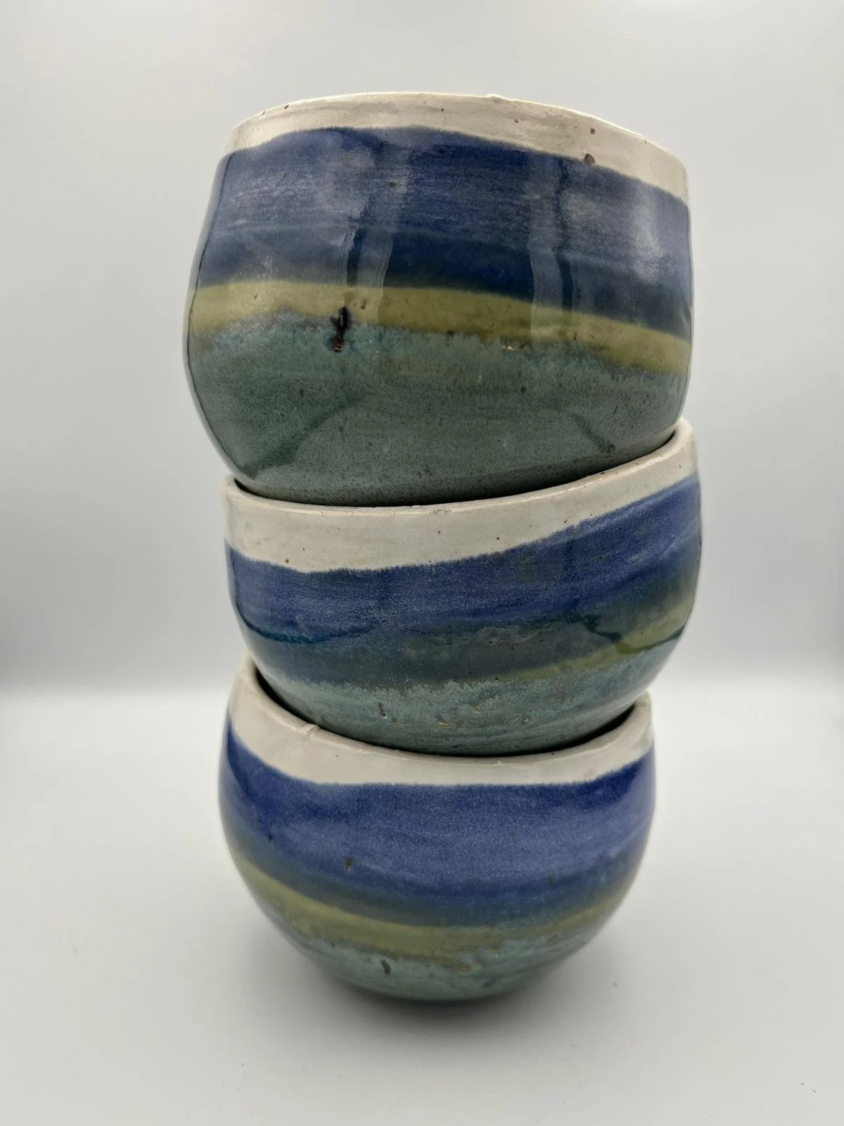 Drie gestapelde keramieken kommen met blauwe en groene strepen op een witte achtergrond.