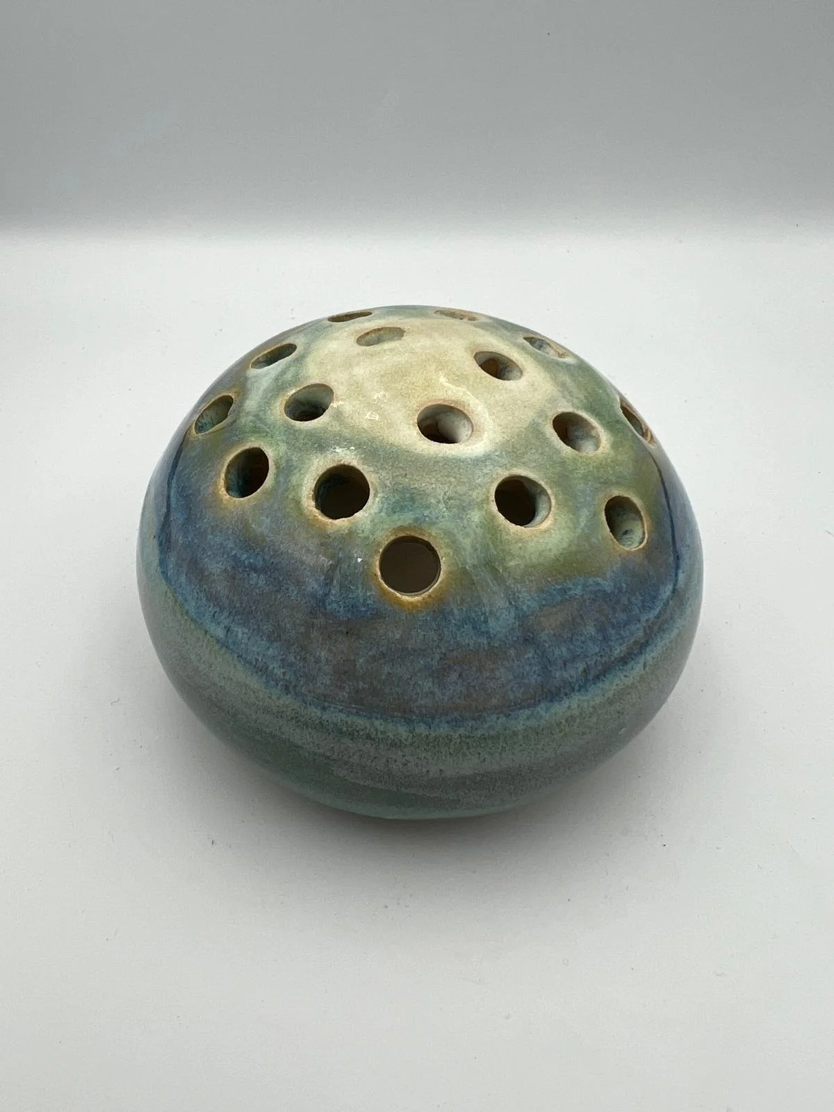 Kleurrijk keramisch object met meerdere ronde gaten, in blauwe en groene tinten.