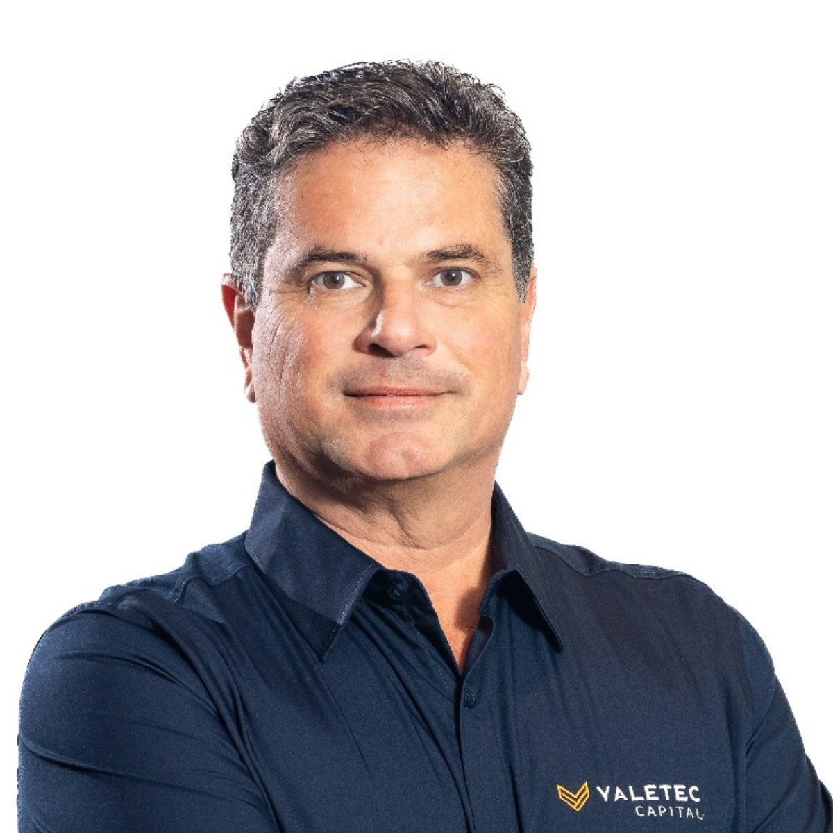 A man with short dark hair and blue eyes, wearing a navy blue shirt with the Valetec Capital logo, looking confident with crossed arms, against a white background.