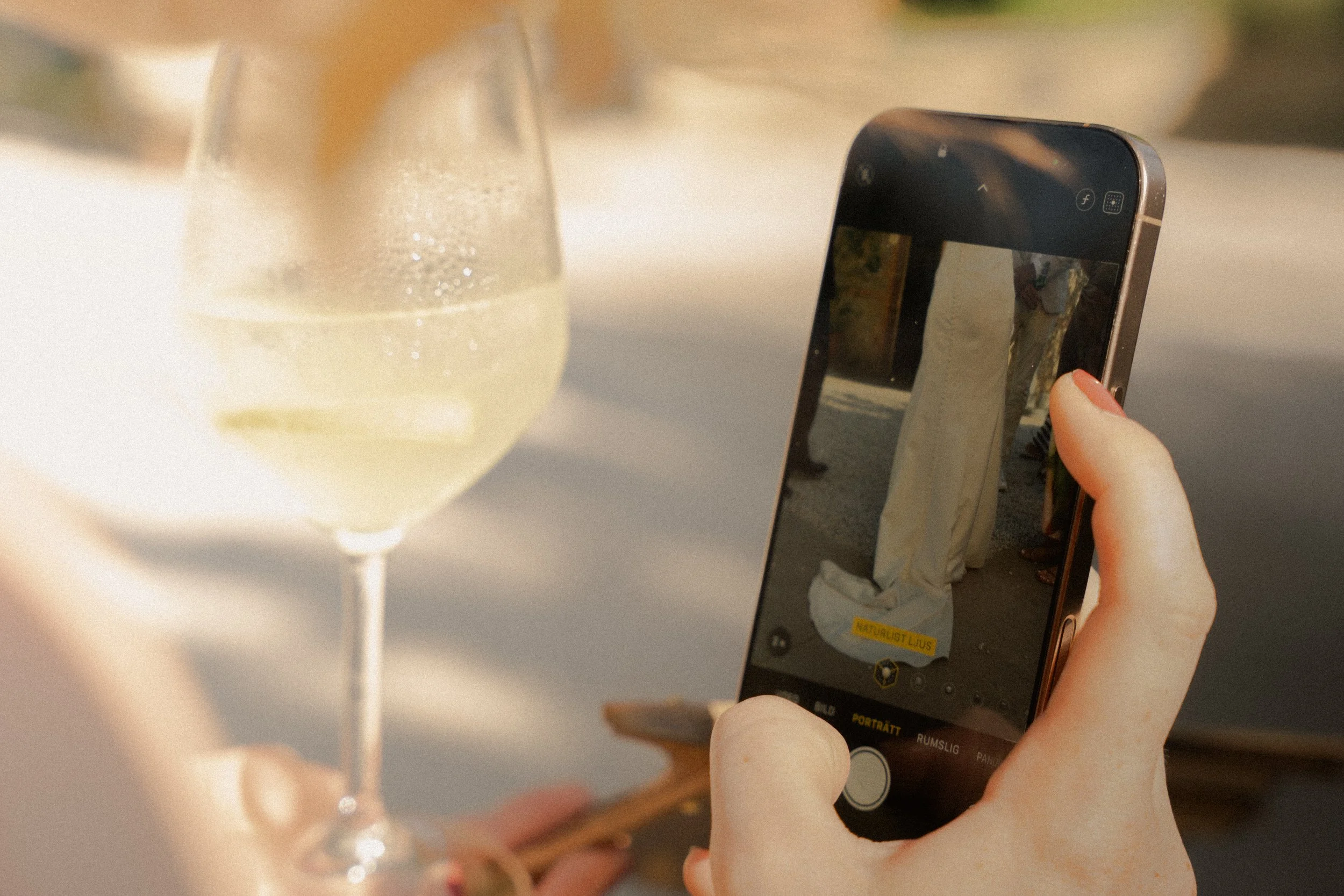 A person holding a smartphone and taking a photo of a glass of champagne with bubbles inside.