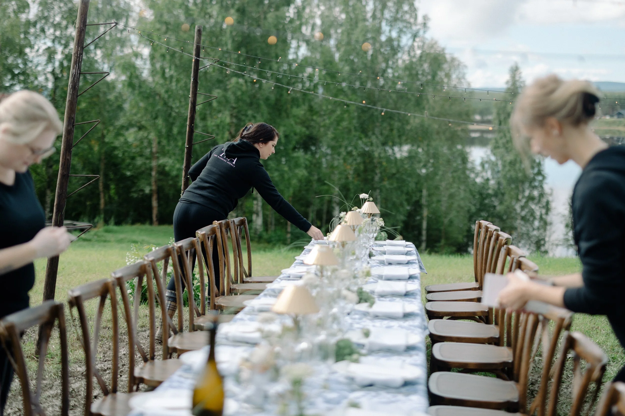 three ladies in black setting a table outdoors