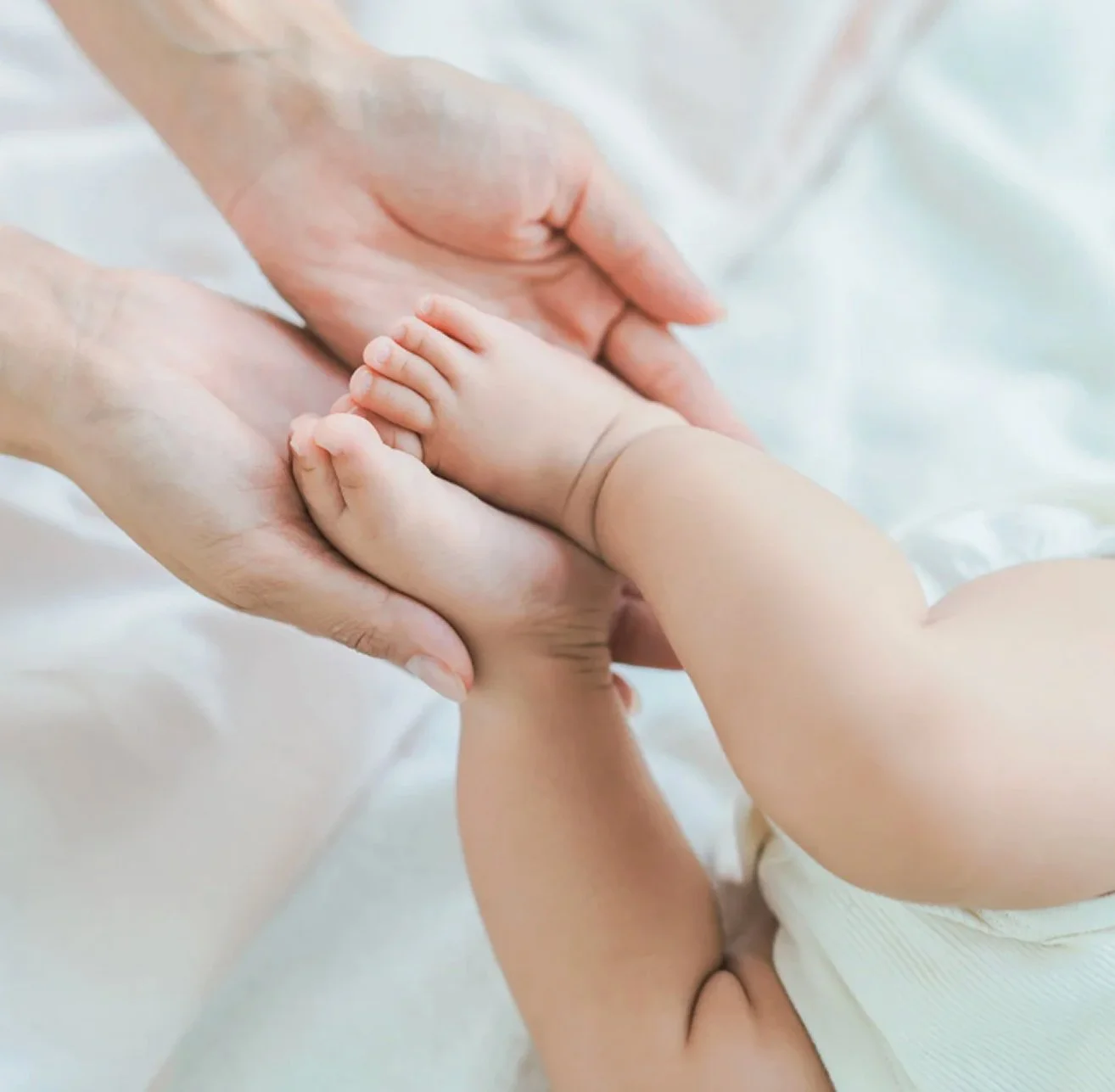 A baby's foot being held gently by an adult's hands.