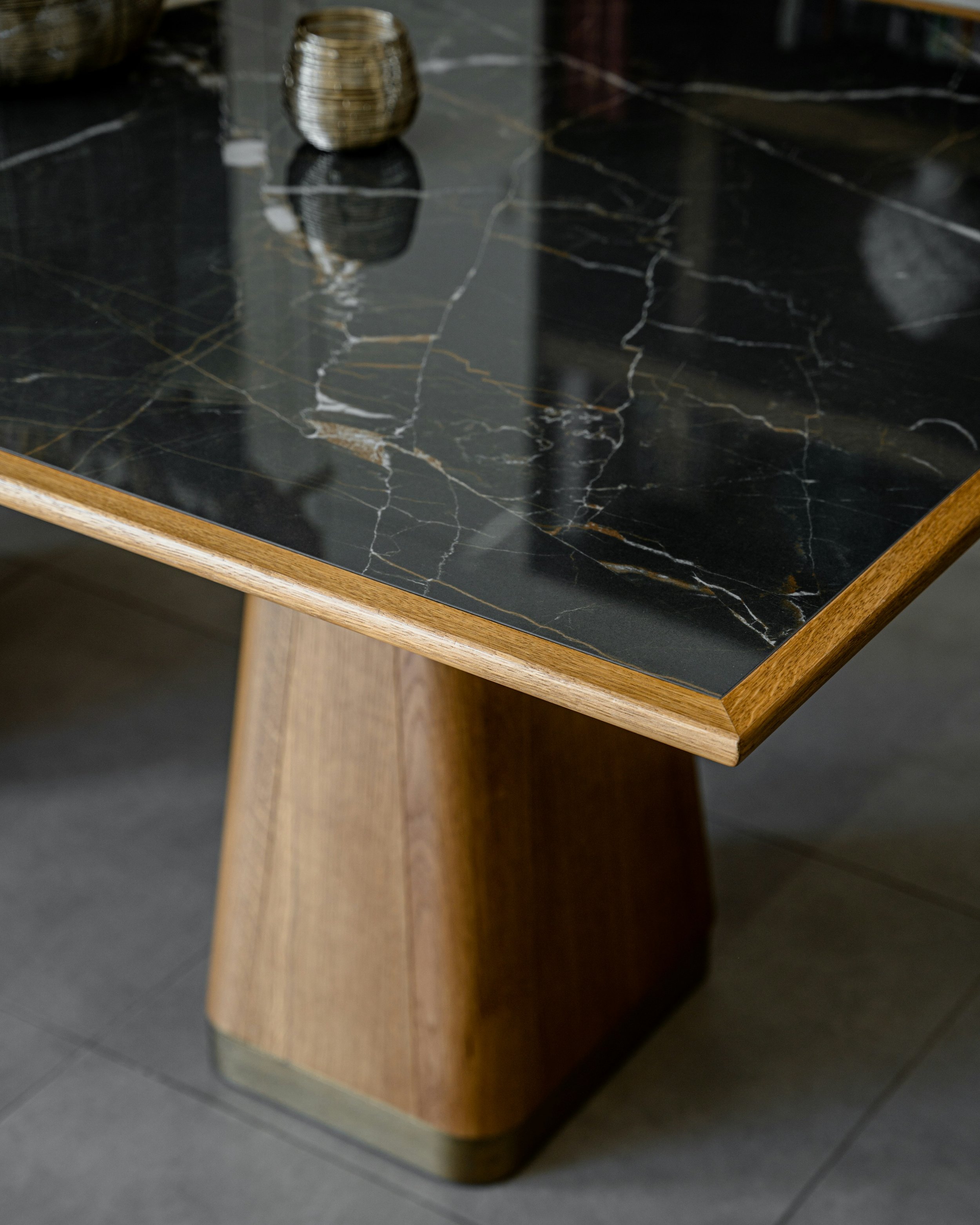 Close-up of a wooden table with a black marble top with gold, white, and gray veining, featuring a rounded wooden base and a reflective surface.