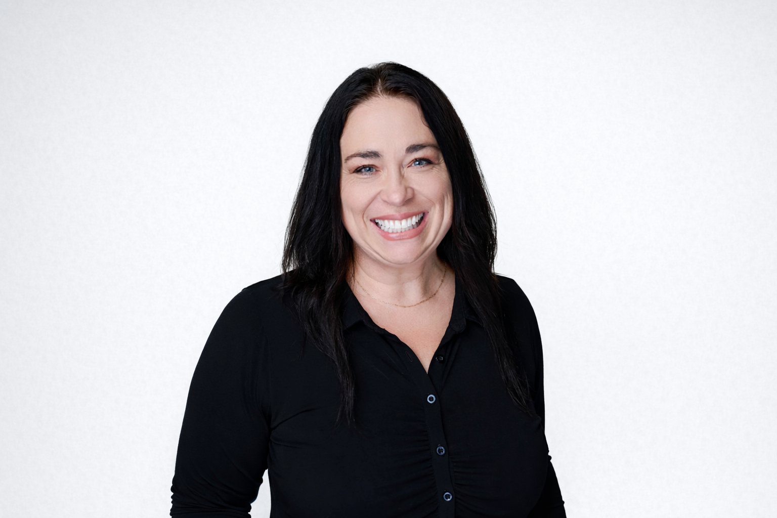 A woman with dark hair smiling, wearing a black shirt, against a plain light background.