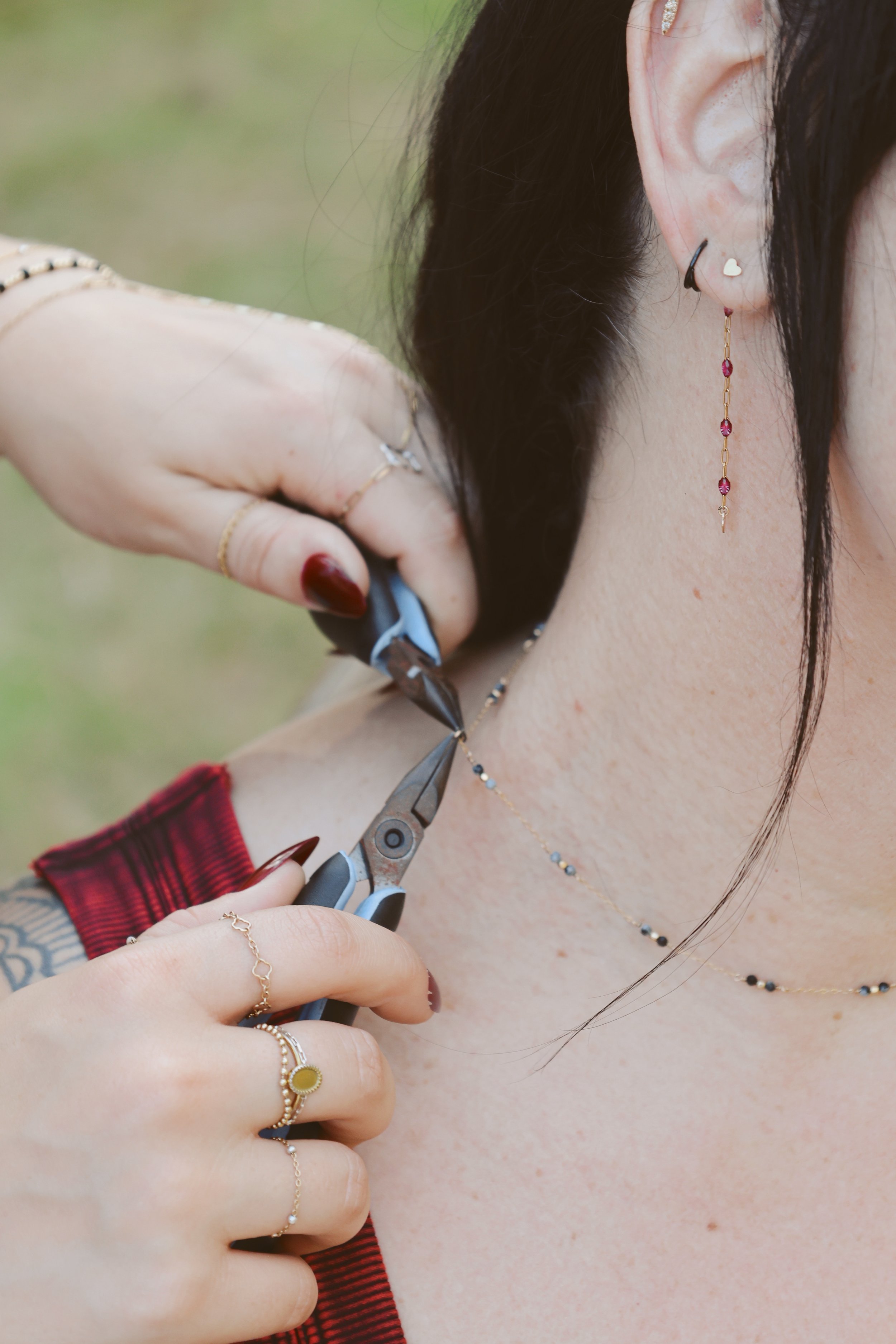 A person cutting a necklace around their neck with a pair of scissors. The person is wearing multiple rings, earrings, and a red garment.