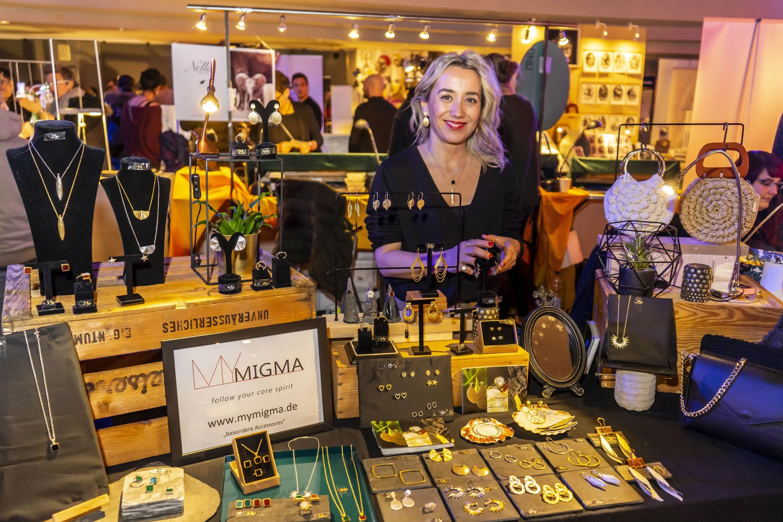 Frau verkauft Schmuck an einem Messestand auf einem Markt, mit verschiedenen Halsketten, Ohrringen, Ringen und anderen Accessoires ausgestellt.