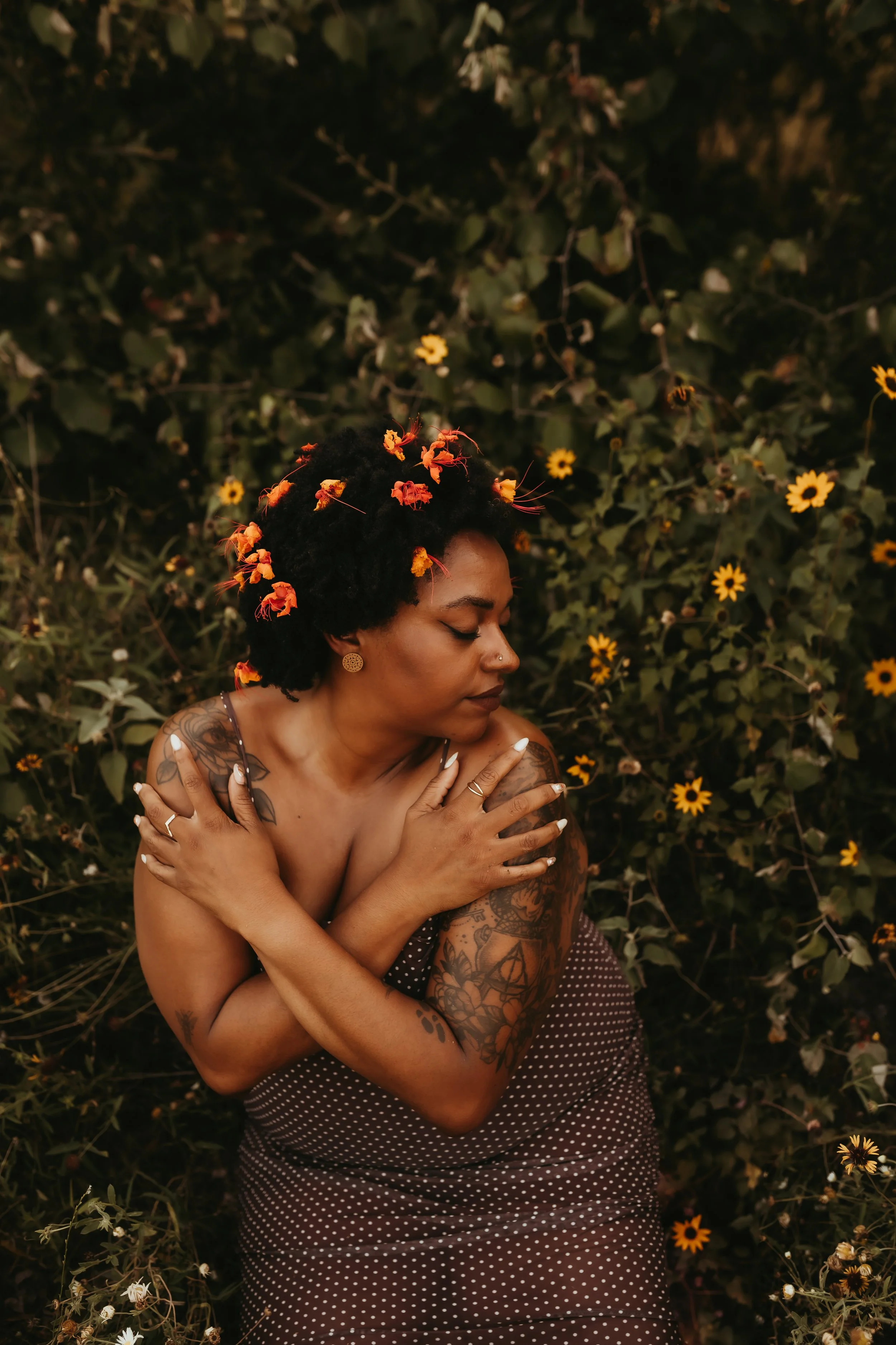 a black woman with flowers in her hair embracing herself.jpg