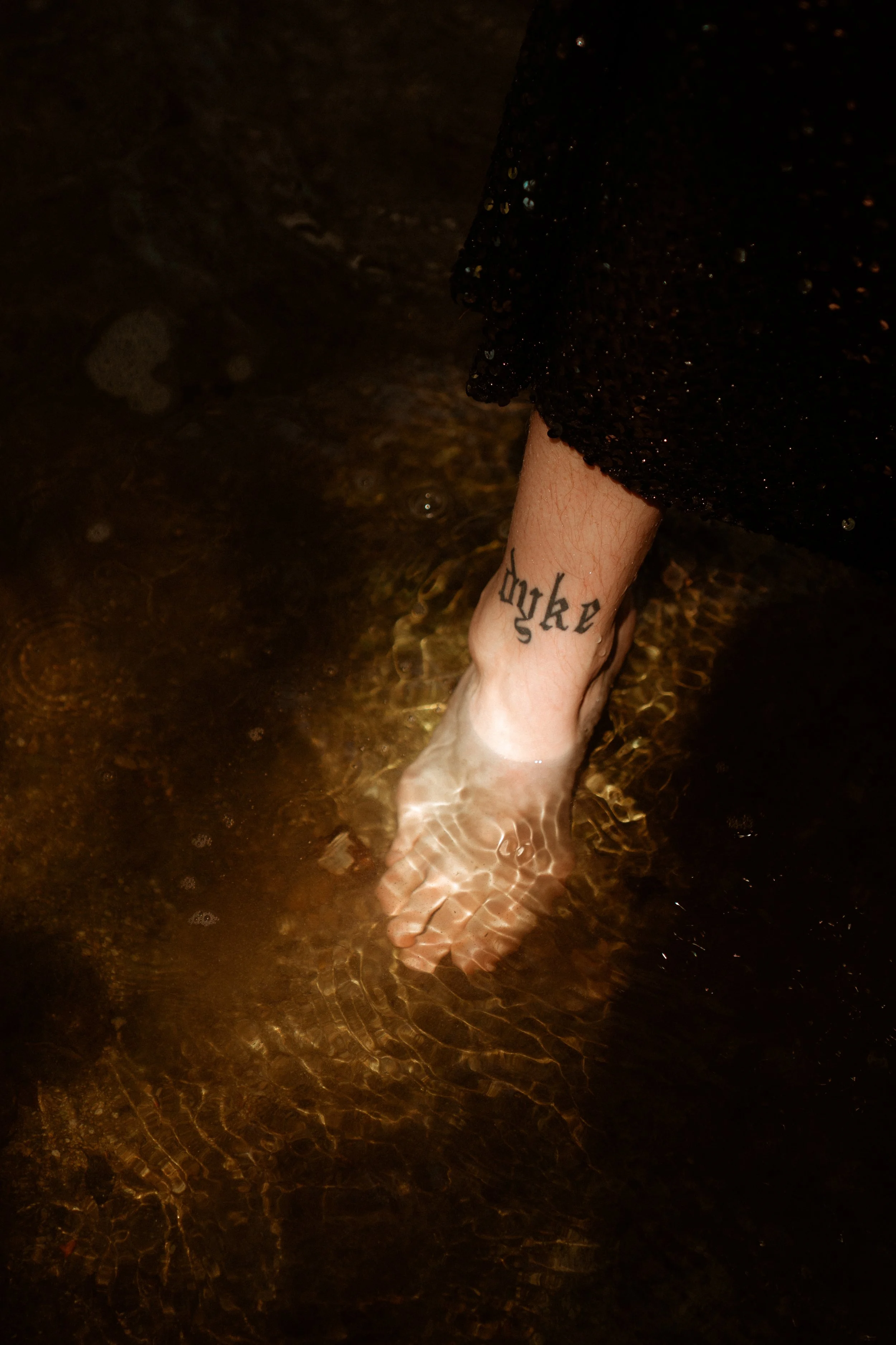 A tattoo on someone's foot that reads "dyke" in gothic font