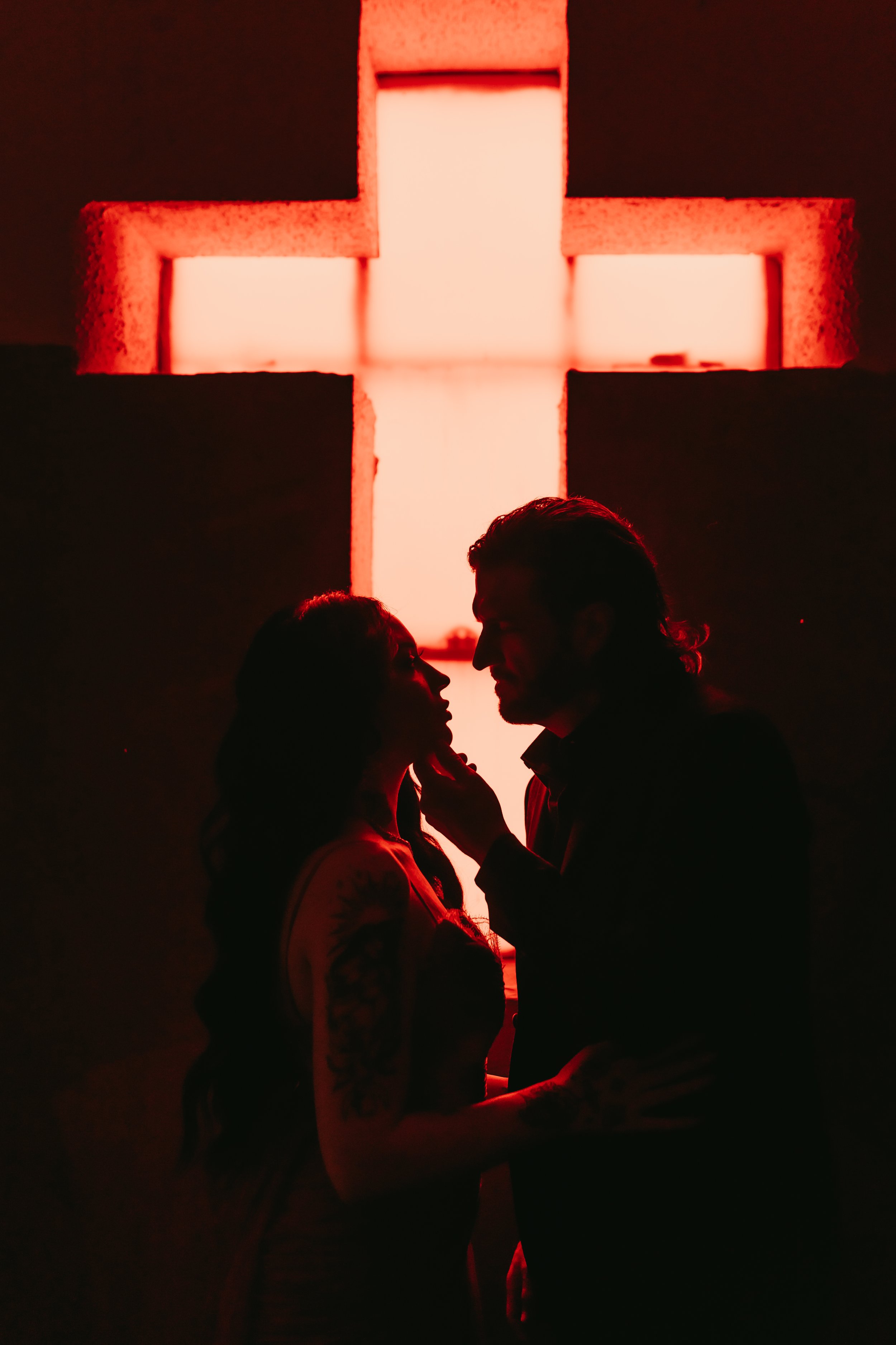a silhouette of a man and woman embracing in front of a red cross in an abandoned church in Houston, Texas