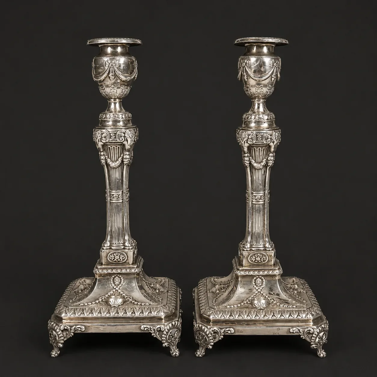 Antique sterling silver candlesticks in the neoclassical style featuring fluted shafts, decorative garlands, and ornate square bases.