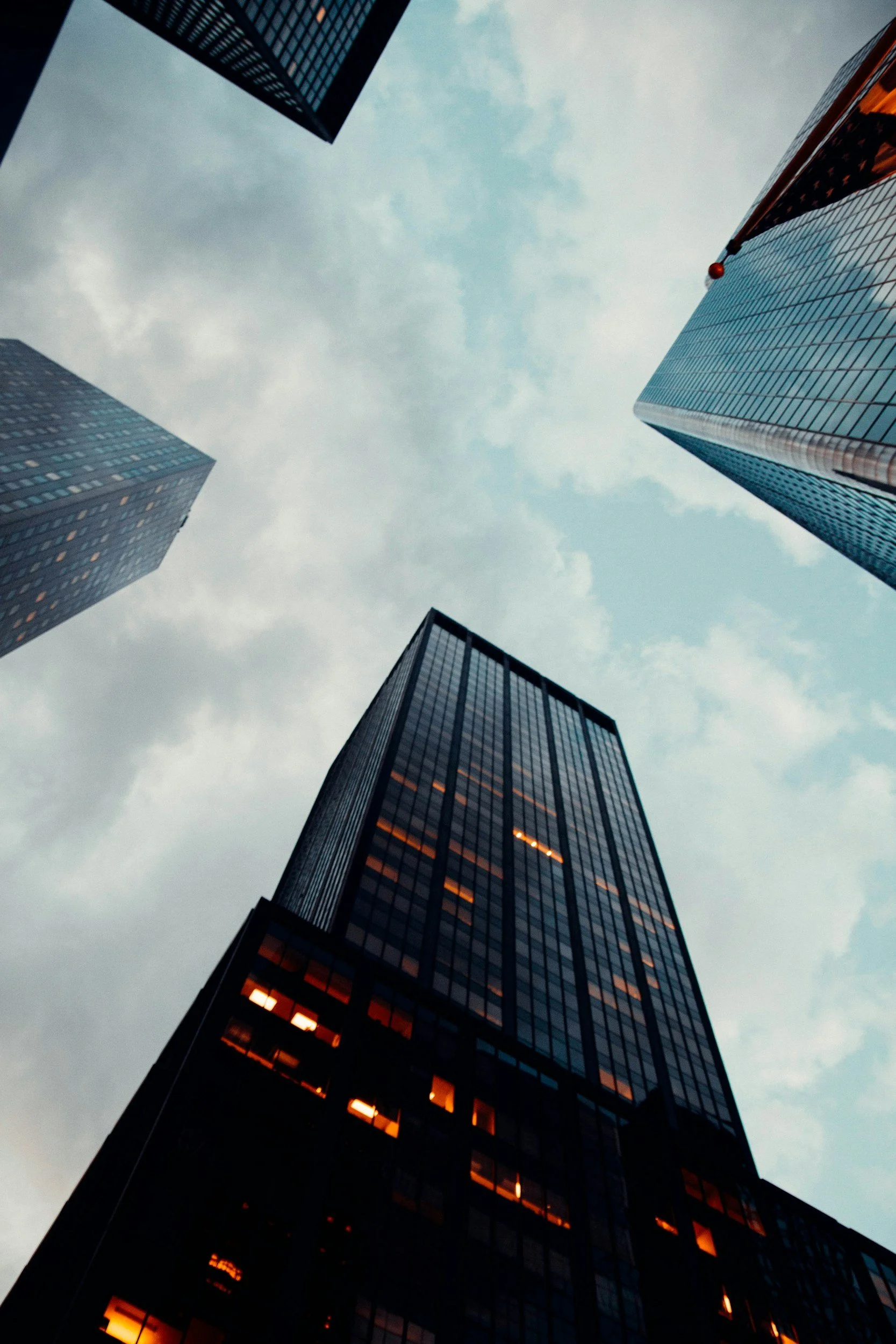 View of tall skyscrapers from ground looking up at cloudy sky.