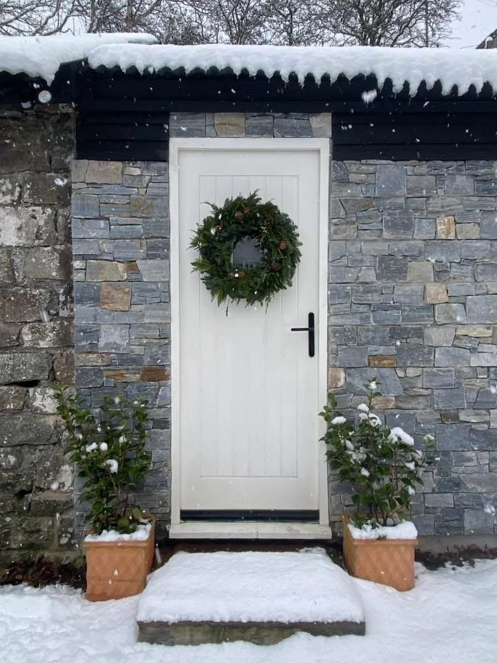 Pet crematorium in south Wales with white door with a wreath, flanked by potted plants, outside in snow.