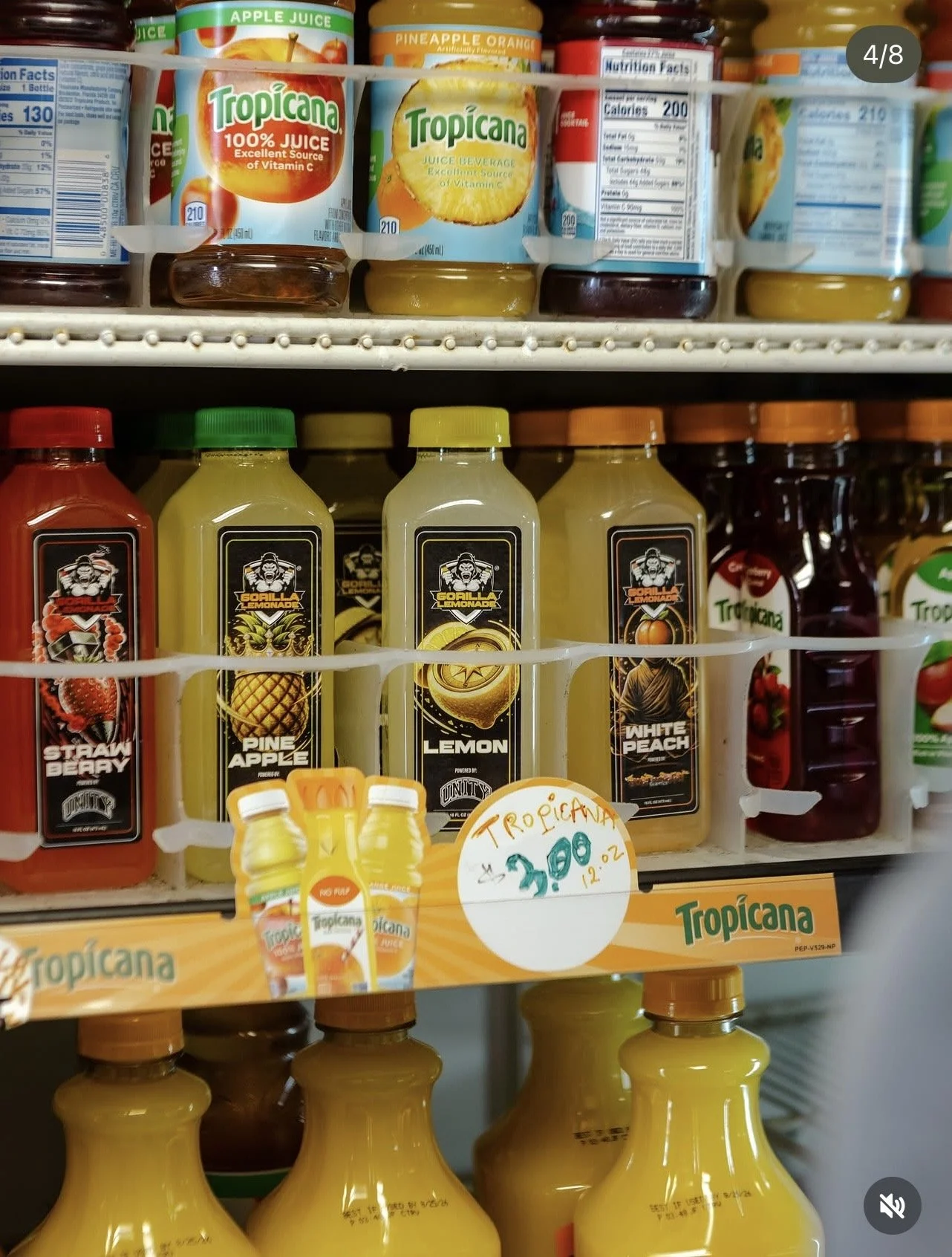 Shelf in a store displaying various bottles of juice and beverages. The top row features Tropicana orange and pineapple juices, with other fruit-flavored juices next to them. The bottom row has bottles labeled 'Gorilla Lemonade,' with flavors like strawberry berry, pineapple apple, lemon, and white peach. Price tag shows $3.00 for Tropicana juice.