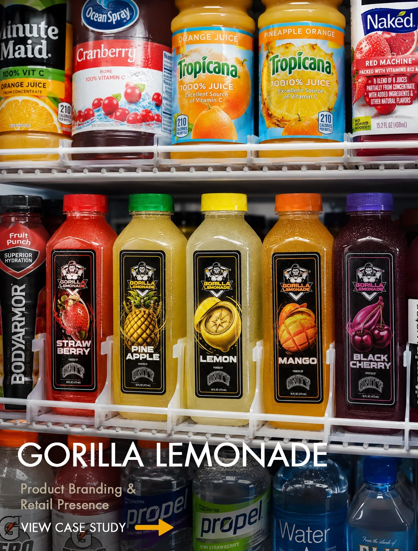 Shelf display of bottled beverages, with pineapple, lemon, mango, and cherry flavored drinks prominently featured. The upper shelf includes orange juice, cranberry juice, and tropical juice bottles. The lower shelf has Gorilla Lemonade bottles in flavors like strawberry, pineapple, lemon, mango, and black cherry, accompanied by Propel water bottles and a water bottle labeled 'From the islands of Fiji.'