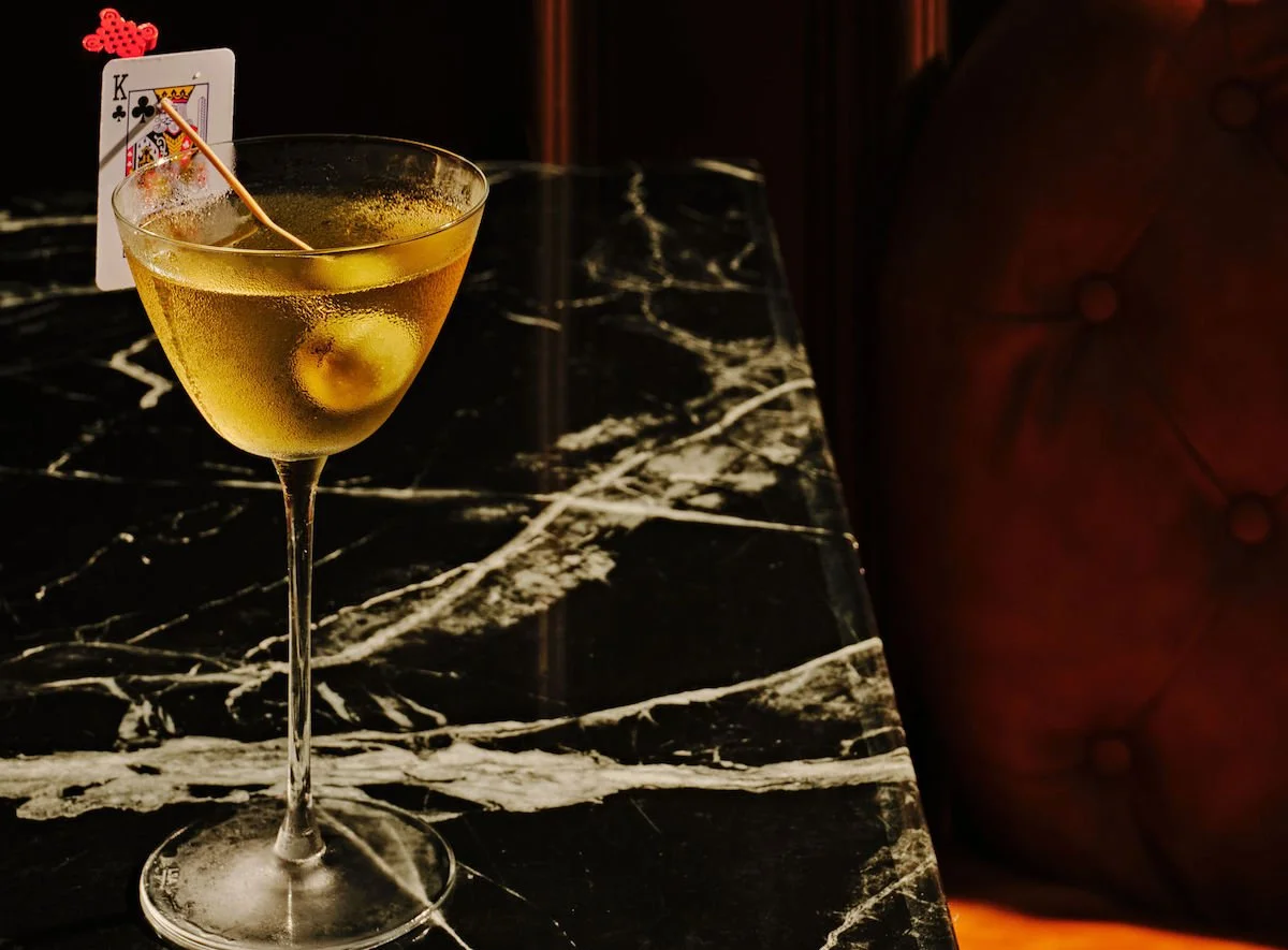 Martini cocktail at Blackjack Bar Tapas in Midtown Atlanta with a playing card garnish on a marble table in a moody lounge setting