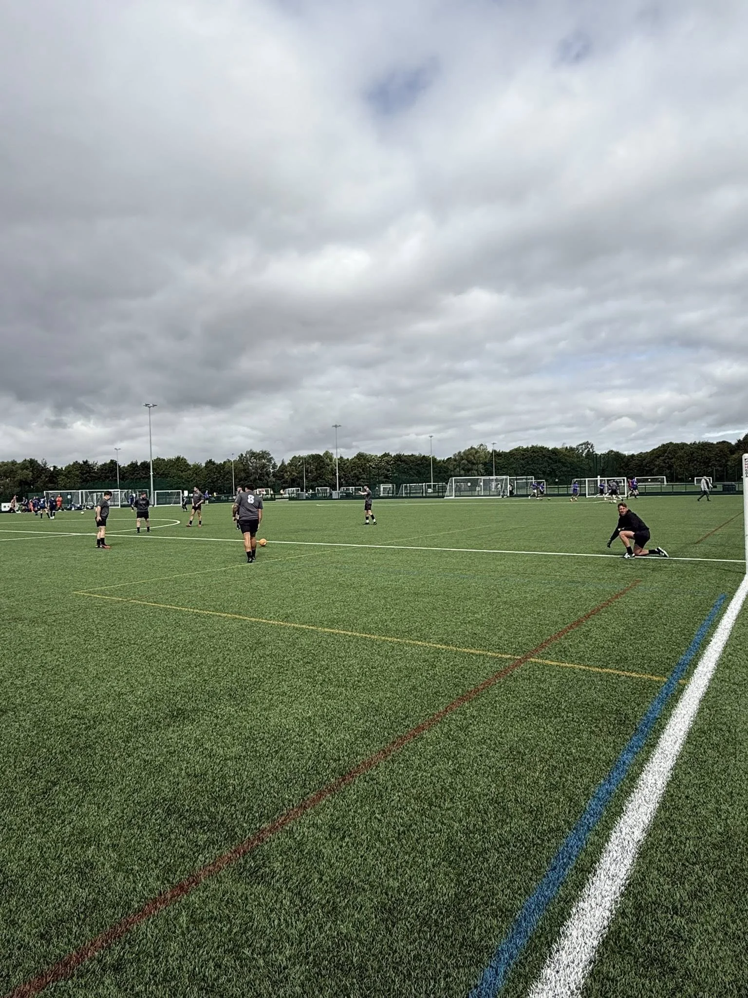 Soccer practice on a green field with players and coaches, cloudy sky