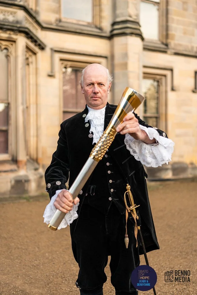 A man dressed in historical black and white costume holding a ceremonial baton outside a castle or historic building.