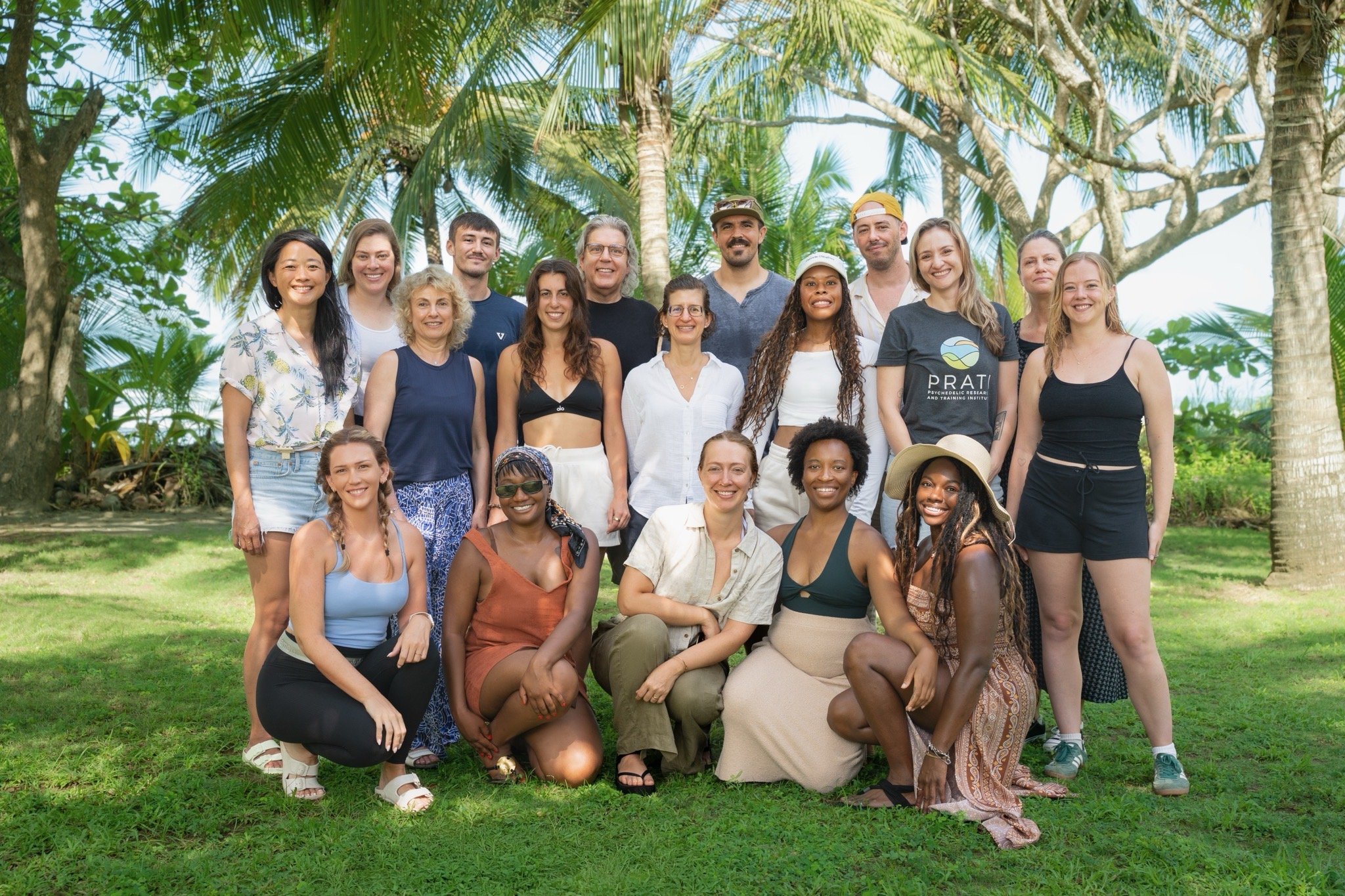 Group of diverse people posing outdoors in a tropical setting with trees and greenery.