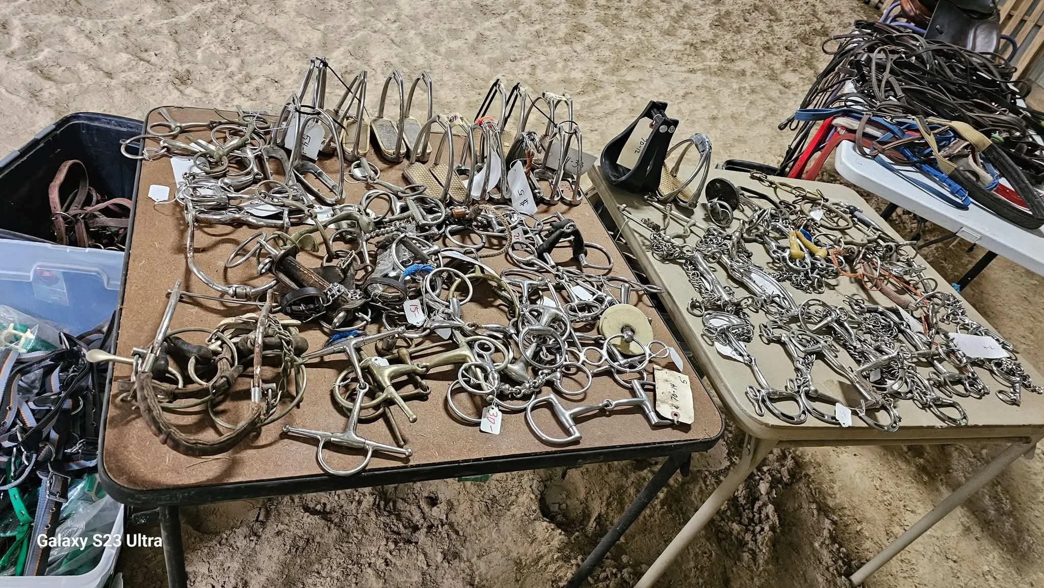 Tables displaying various horse bits and bridles at a marketplace or store, with tags and organized sections.