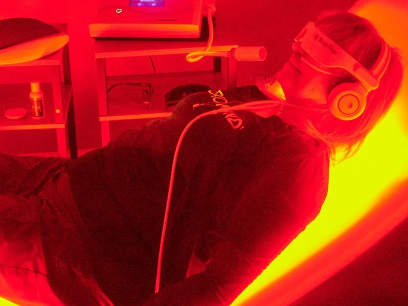 A woman lying under a red light therapy lamp with a relaxed expression.