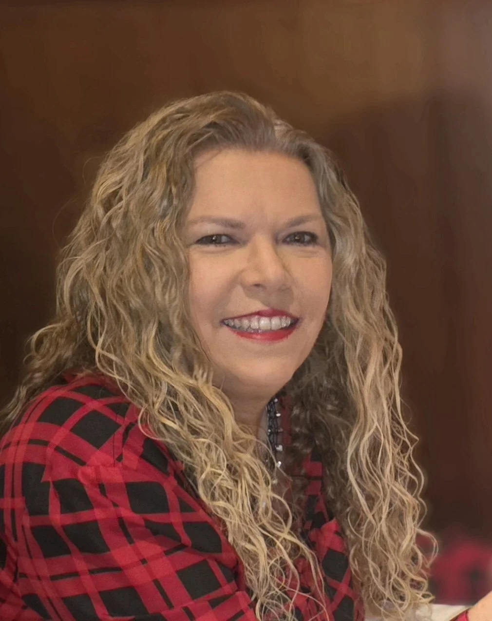 Woman with curly blonde hair smiling, wearing a floral dress.