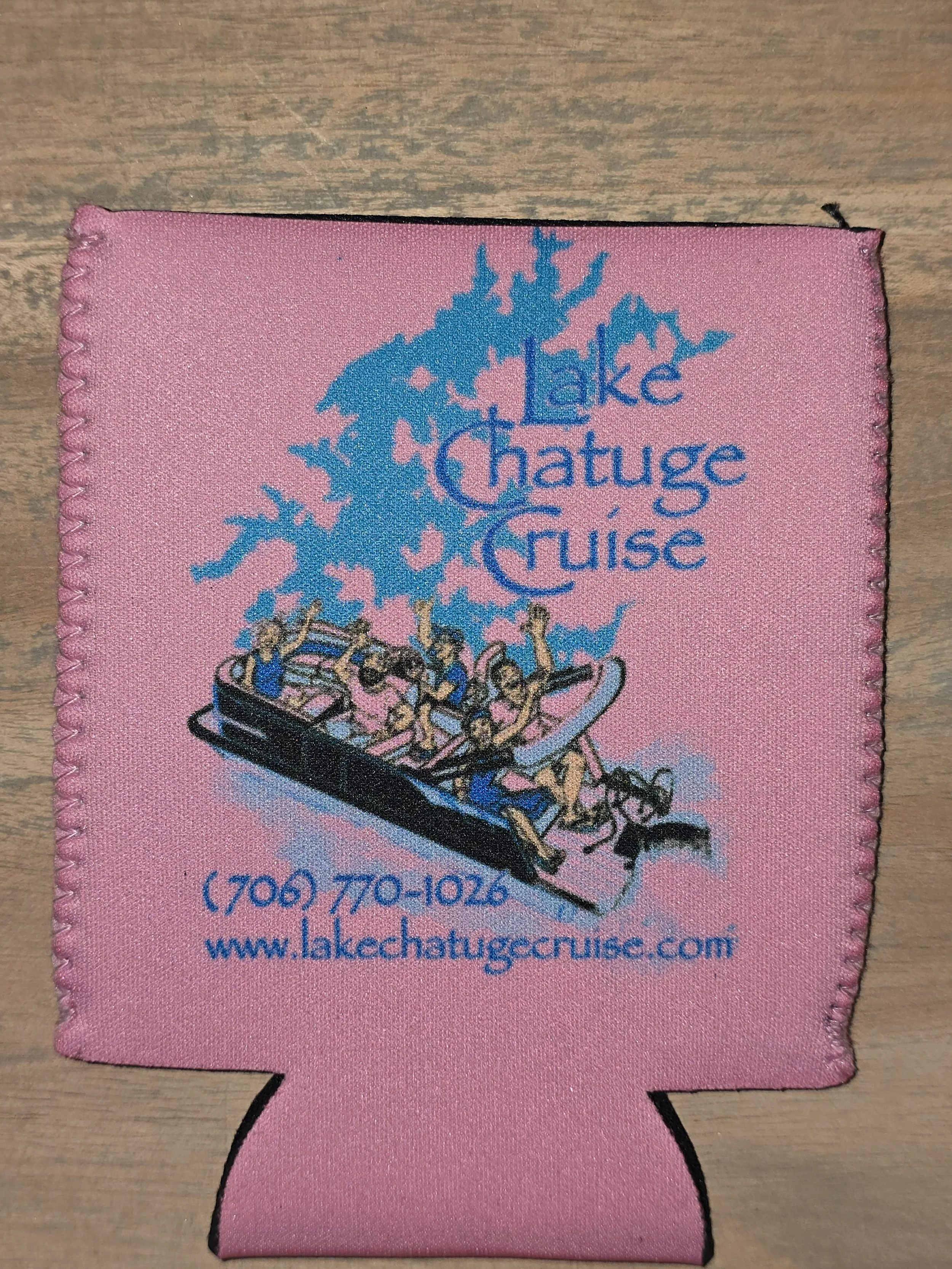 Pink fabric item with blue and black printed logo for Lake Chatuga Cruise, showing people riding a boat with a wakeboard in hand, you can see a phone number and website at the bottom.