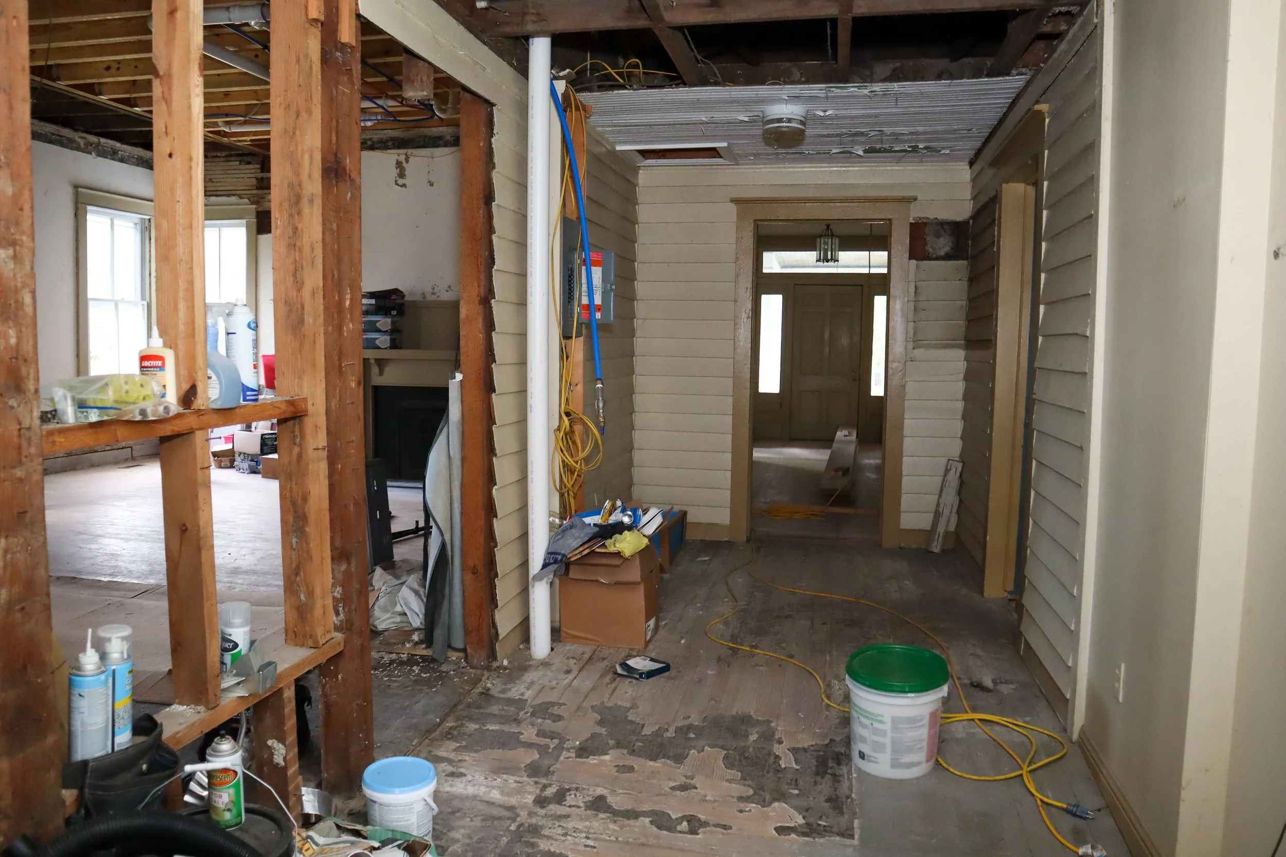 Interior of a house under renovation, featuring exposed wooden beams, construction materials, and a partially finished hallway.