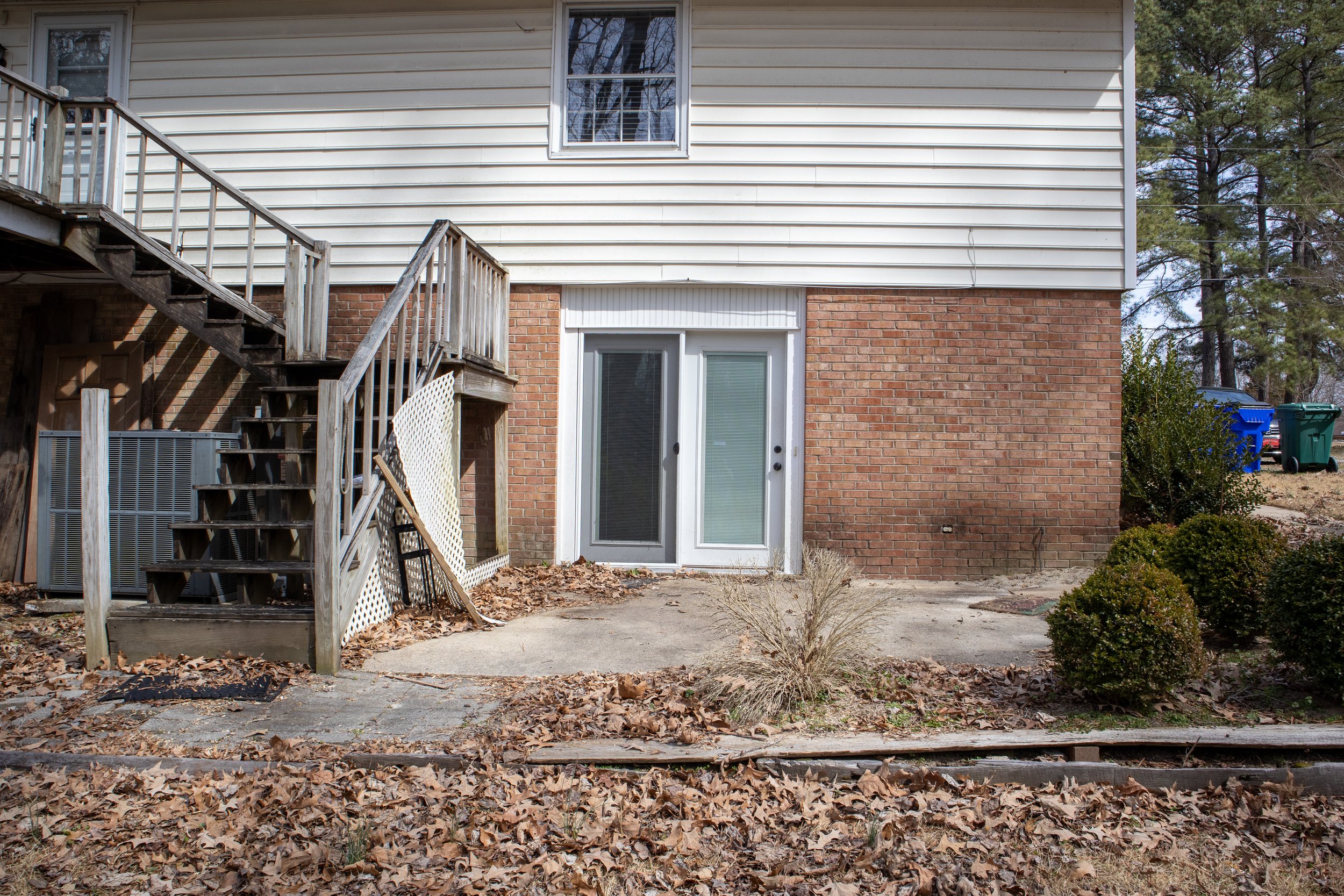 Backyard scene with wooden staircase, brick wall, sliding glass door, and surrounding foliage.