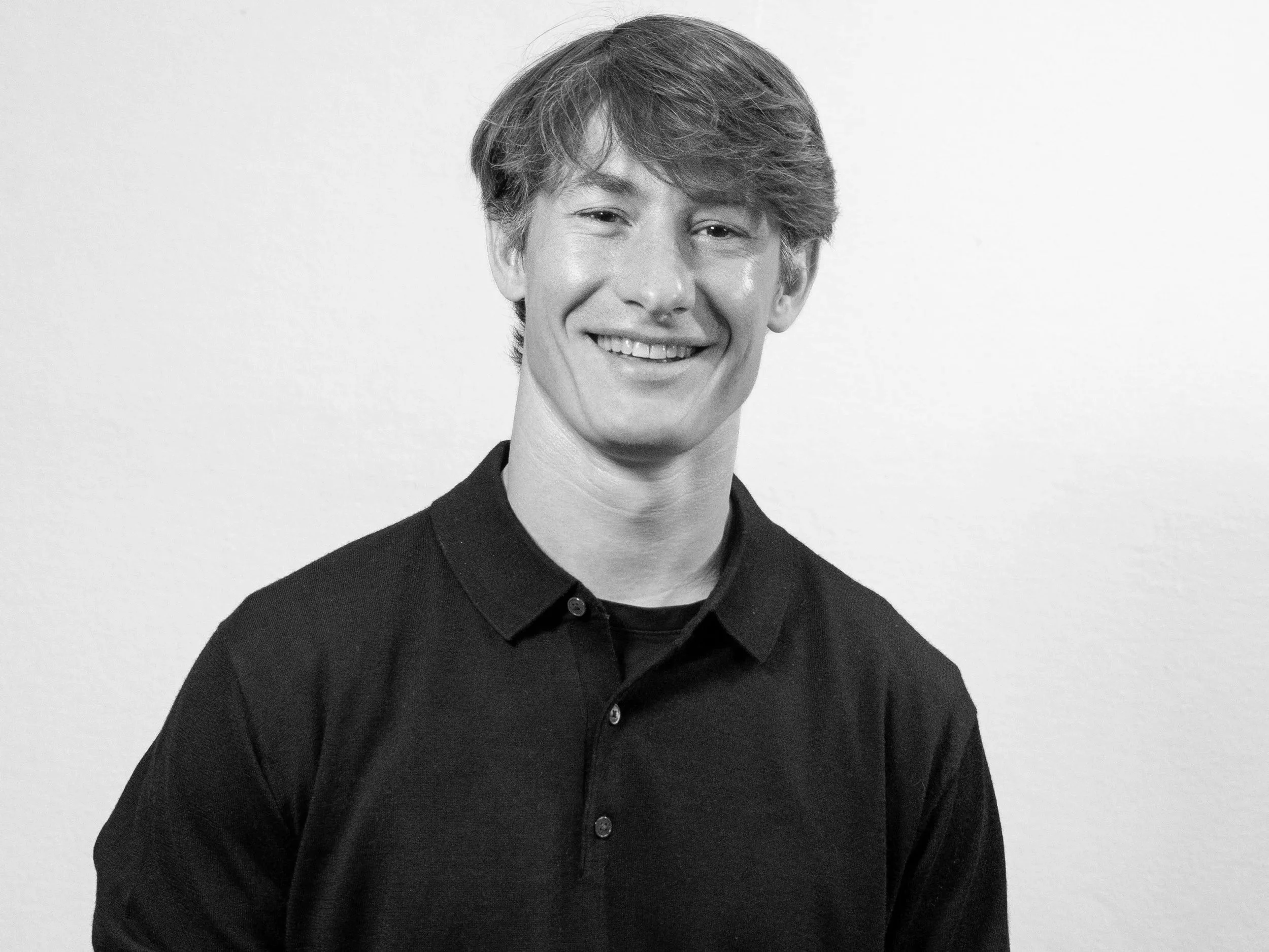 Black and white portrait of a young man with wavy hair, smiling, wearing a collared shirt, against a plain background.
