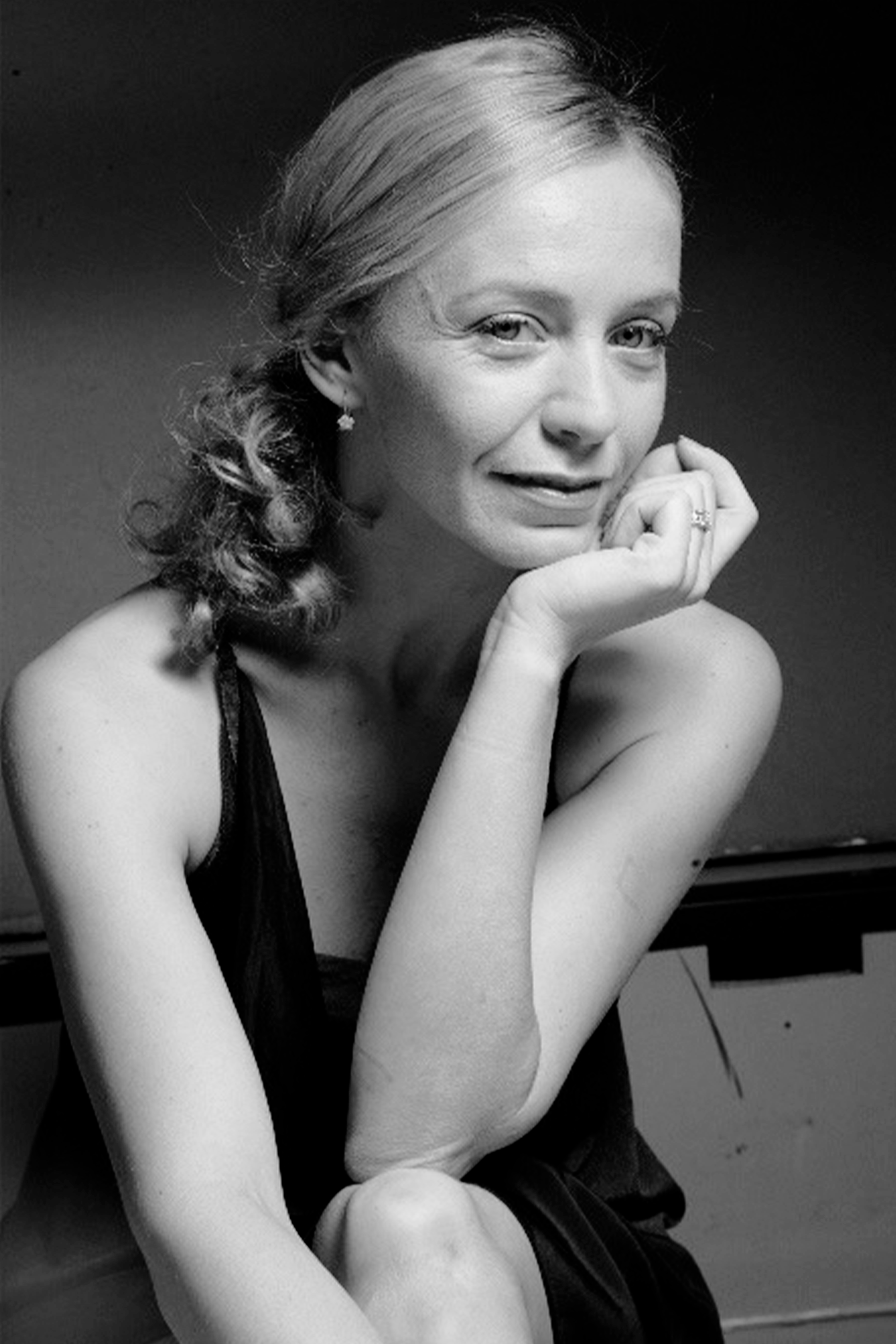 Black and white portrait of a woman with curly hair, resting her chin on her hand, wearing a sleeveless top.
