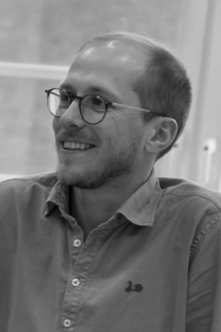 A man with glasses, short hair, and a beard smiling in a casual setting.