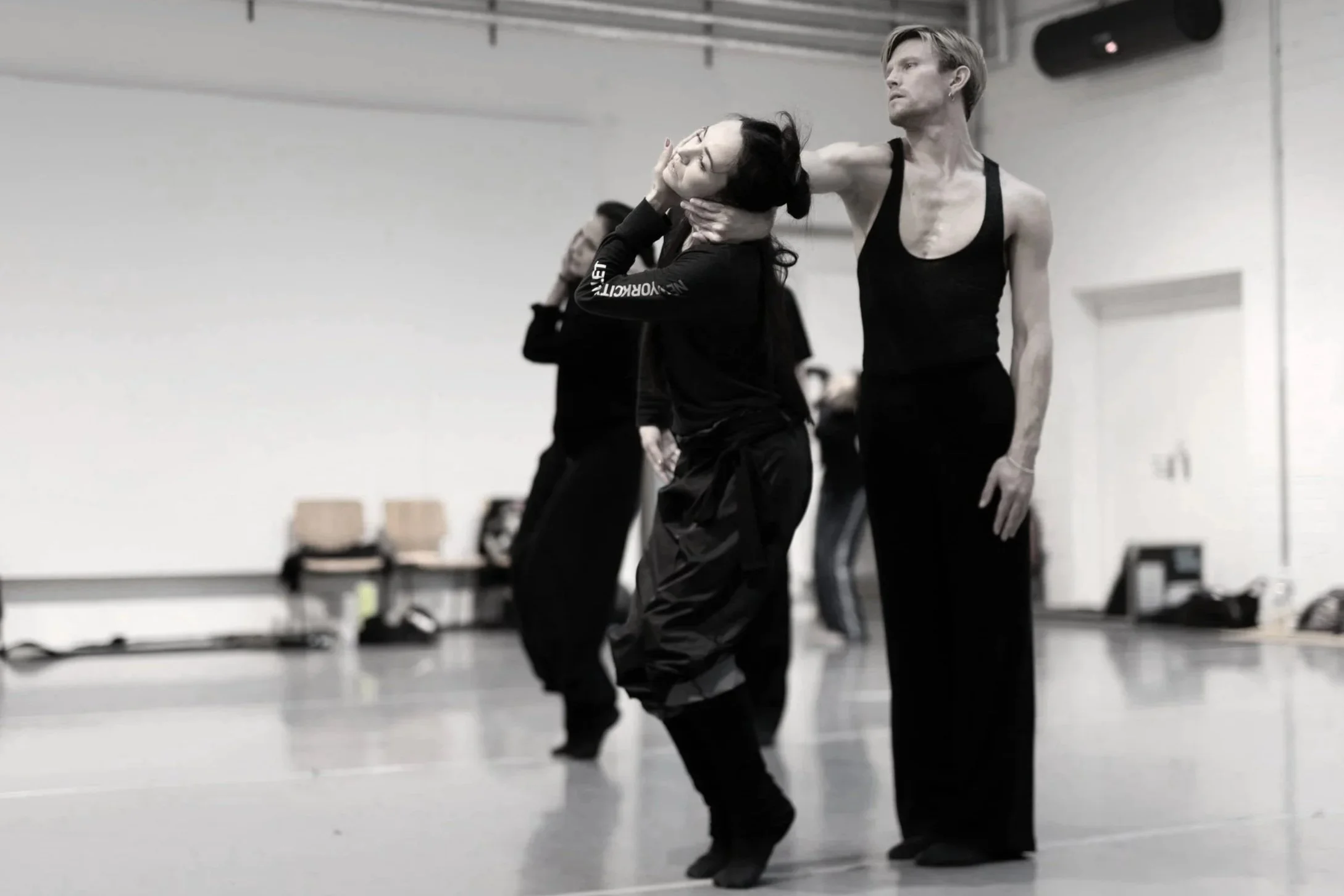 Two dancers practicing in a dance studio with one woman placing her hand on her head and the other assisting her.