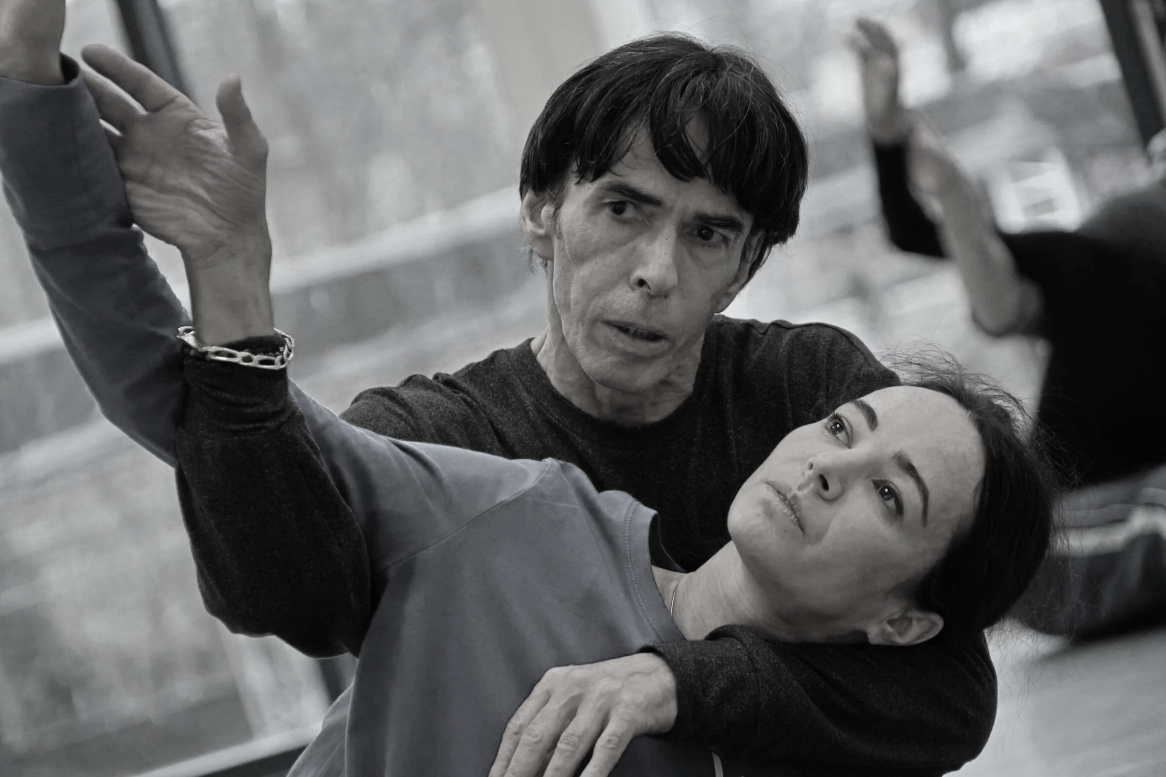 Black and white photo of a man and woman practicing martial arts or self-defense techniques together, indoors, with the man demonstrating a move while the woman observes and listens.