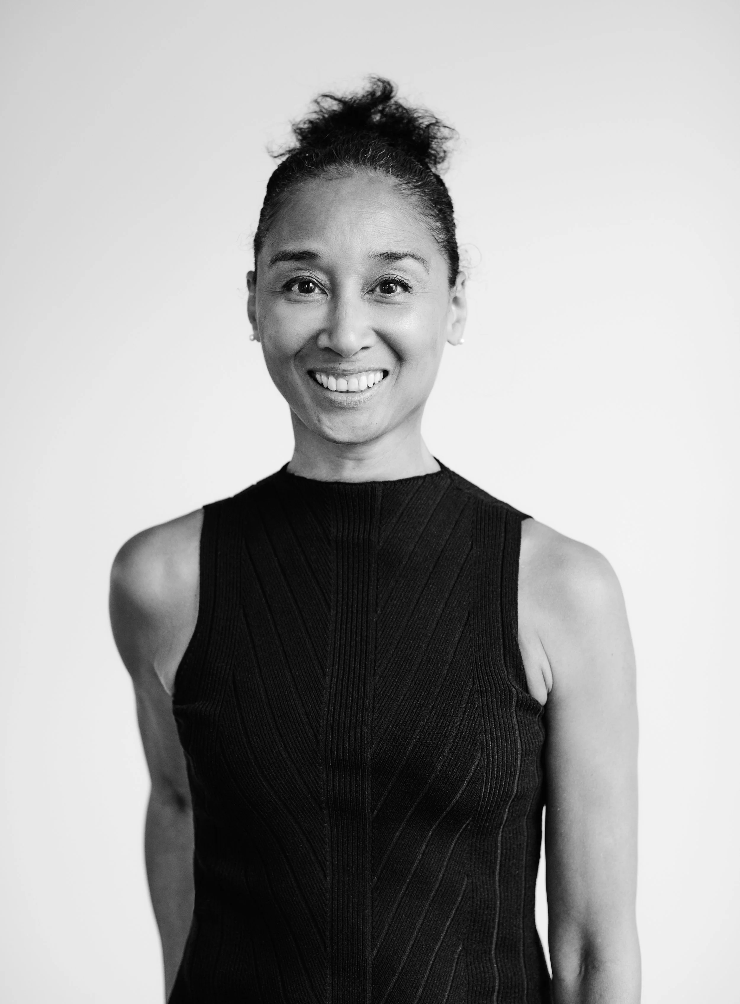 Black-and-white portrait of a smiling woman wearing a sleeveless black top, with her hair styled in an updo, against a plain light background.