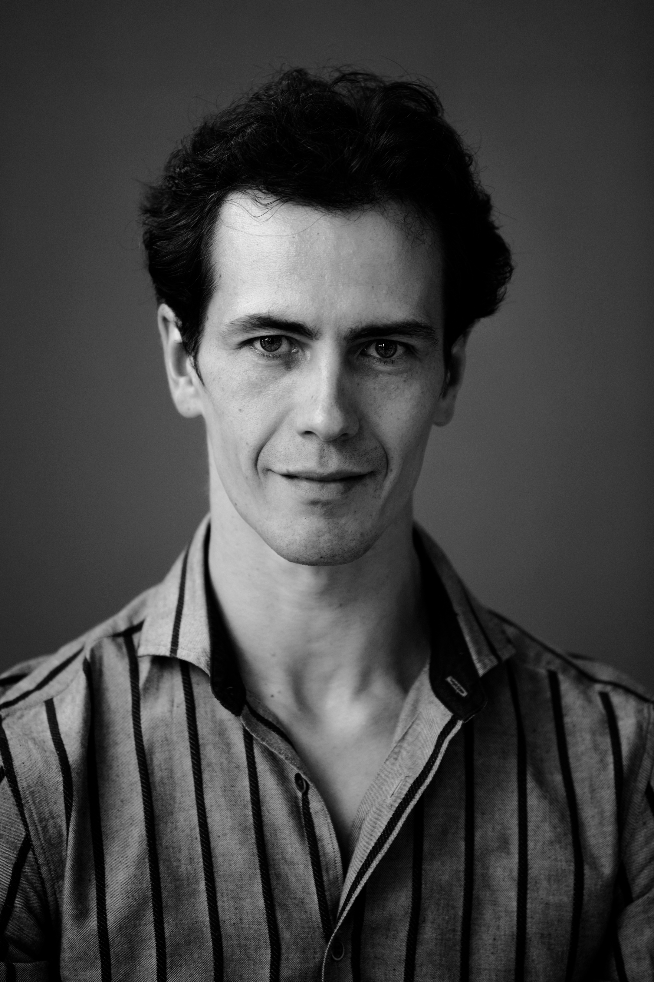 Black and white portrait of a man with dark wavy hair wearing a vertically striped shirt.