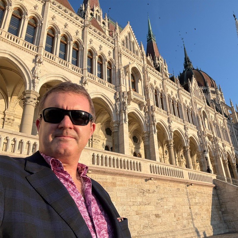 Man in sunglasses standing in front of a historic building with Gothic architecture, featuring pointed arches and spires.