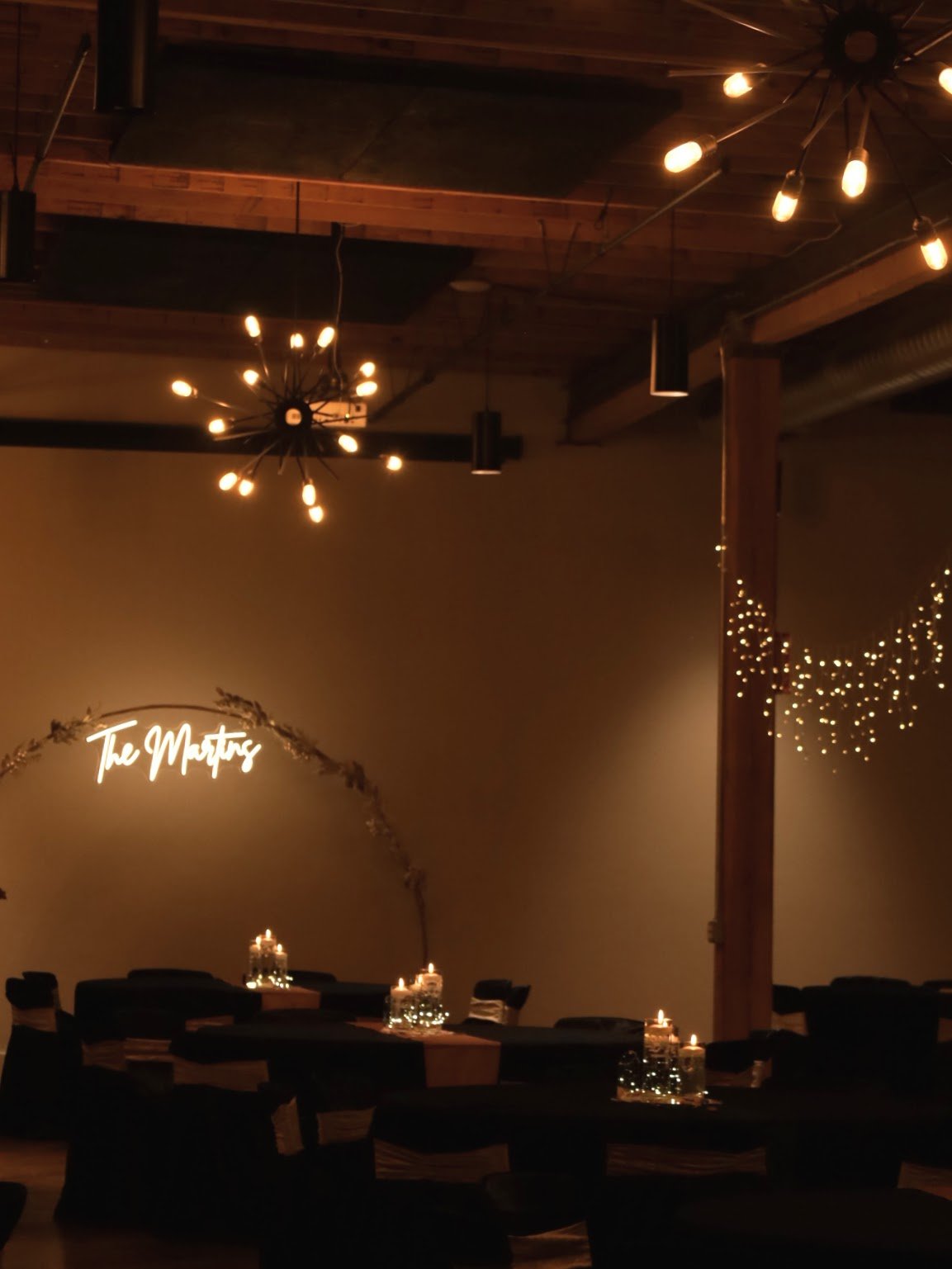 Dimly lit venue with chandeliers, decorated tables with candles, and wall lights spelling 'The Masters'.