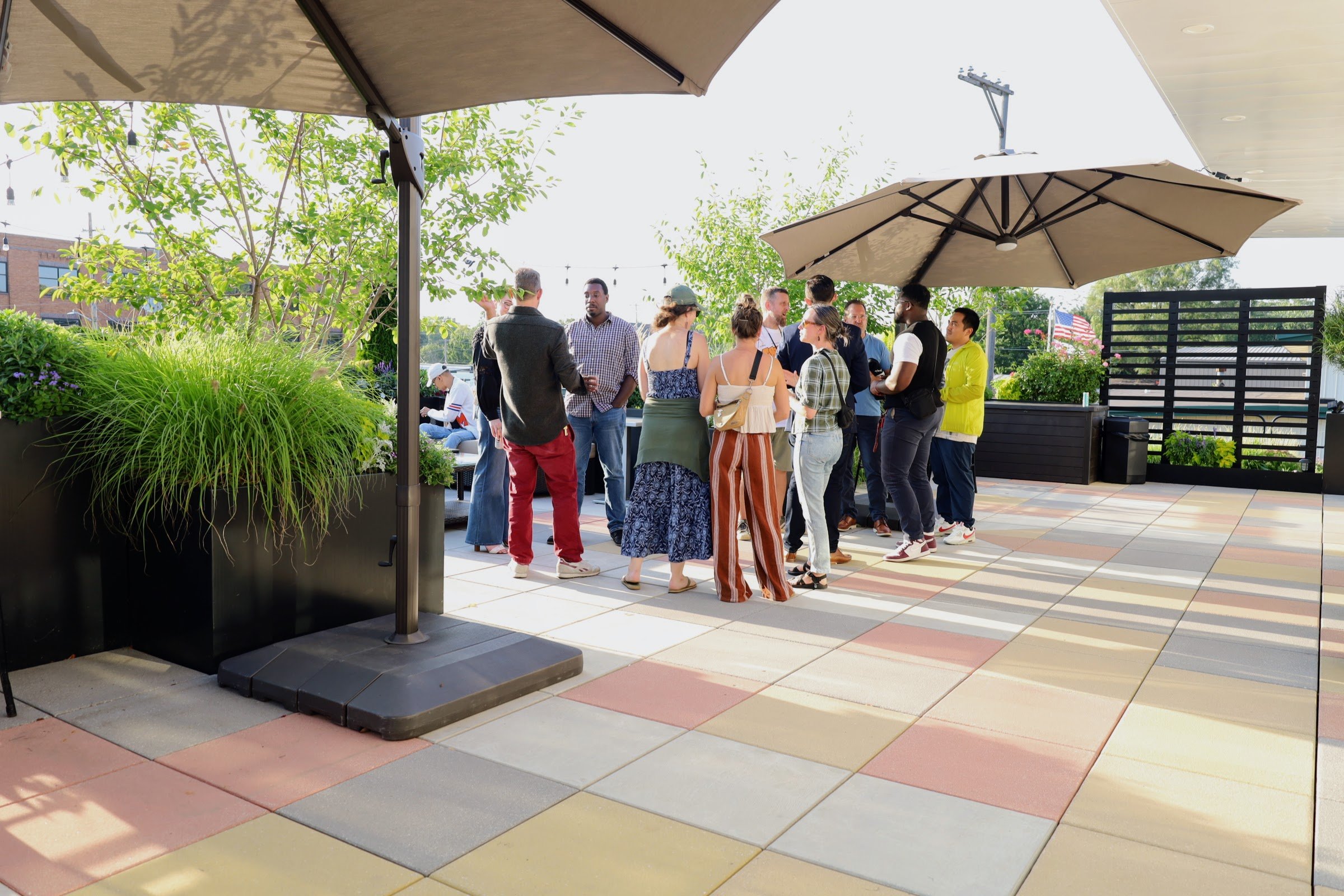 Group of people socializing on a rooftop patio with plants and umbrellas