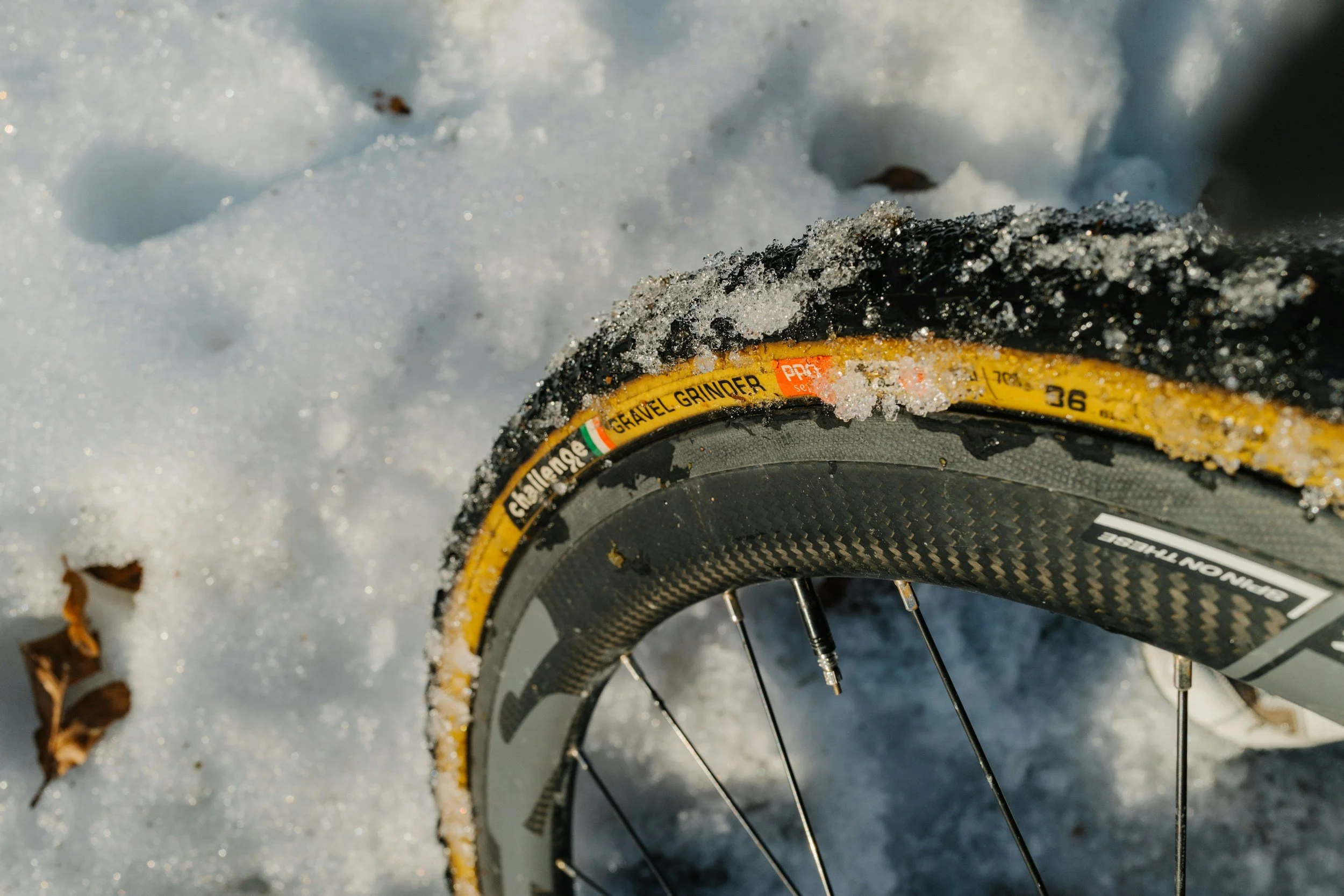 Close-up of a bicycle wheel with snow and ice on the tire and surrounding snow on the ground.