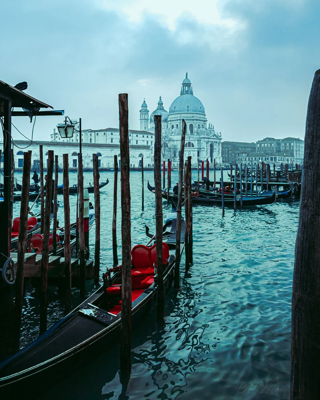 Santa Maria della Salute in Venice under a moody, cloudy sky, with green and blue tones highlighting the architecture against the lagoon.
