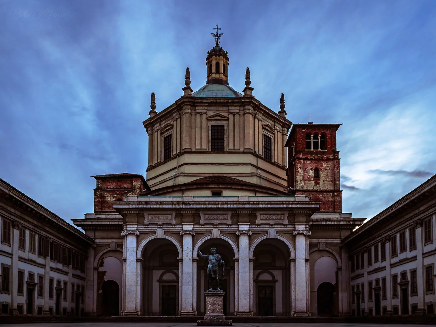 Dramatic sunrise over San Lorenzo in Milan on a windy morning, captured in a long exposure shot with intense blue skies and deep brown architectural tones.
