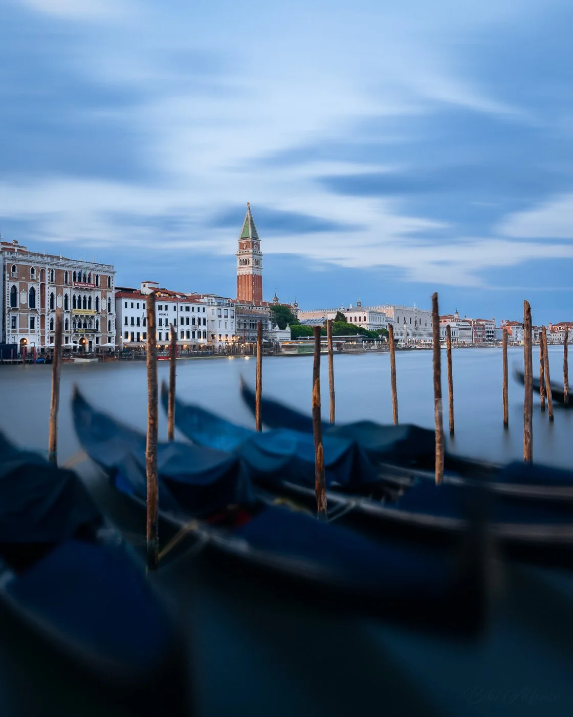 A 120-second long-exposure photograph of Venice at sunset, with blurred gondolas in the foreground, soft blue tones, and the Campanile rising above the waterfront.