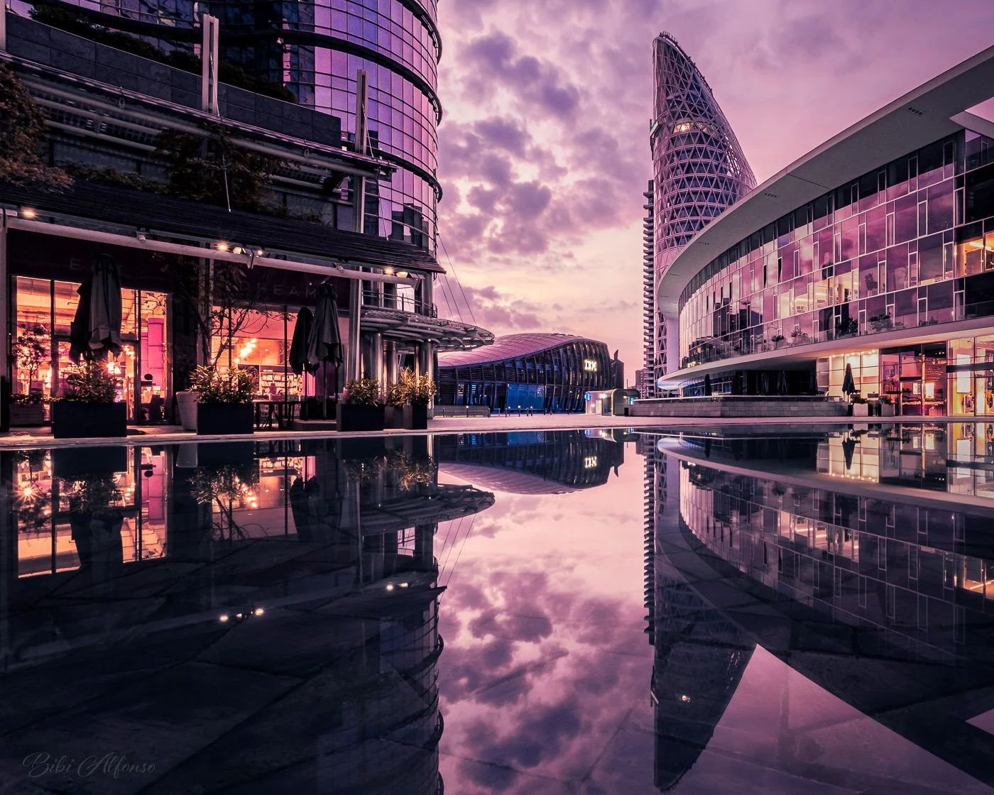 Pink sunrise illuminating Piazza Gae Aulenti in Milan, with reflections of modern architecture against a pink and gold sky.