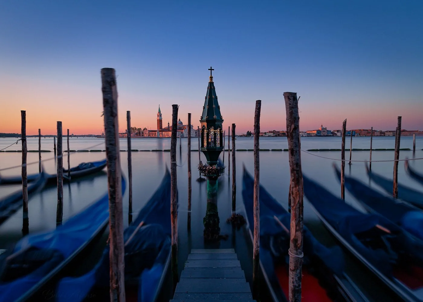 Long exposure shot at sunrise, with moving gondolas in the foreground and the Island of San Giorgio Maggiore in the background, capturing the motion and calm of Venice’s canals.
