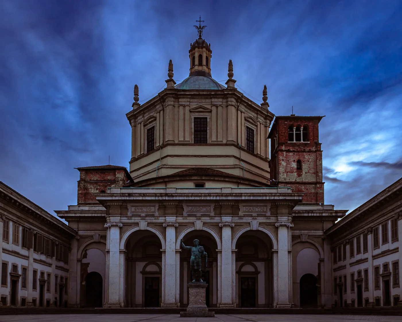Dramatic sunrise over San Lorenzo in Milan on a windy morning, captured in a long exposure shot with intense blue skies and deep brown architectural tones.
