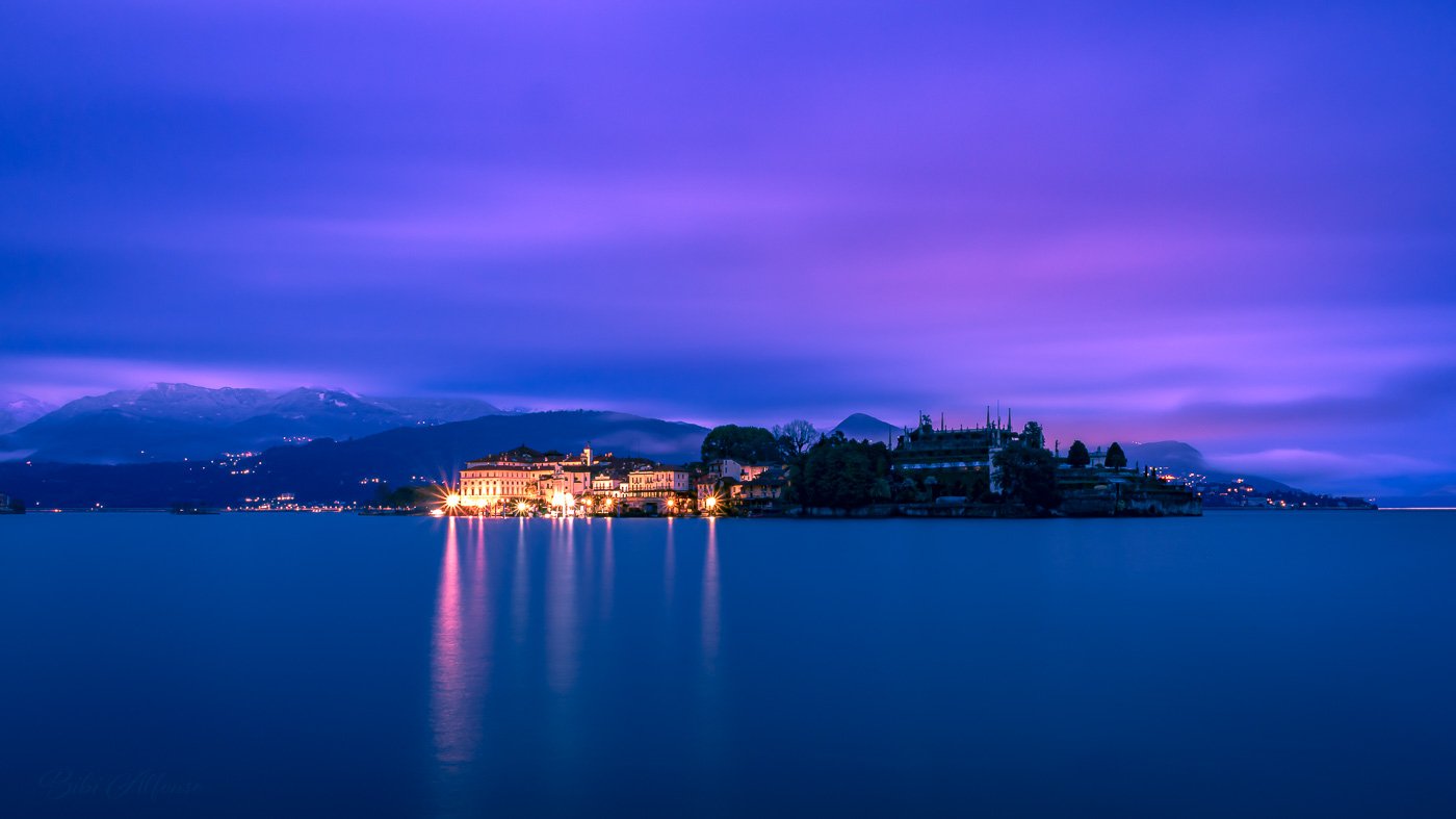 Eight minutes blue-hour long exposure of Isola Bella on Lake Maggiore before dawn, with streaky clouds, a deep blue–purple sky, and the island softly illuminated by artificial lights.