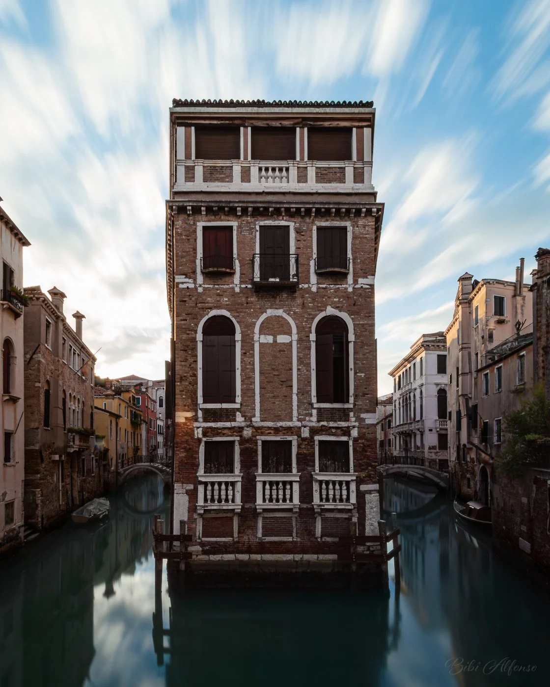 Early morning view of Palazzo Tetta in Venice, situated at the intersection of two canals with blurred, smooth water and soft clouds streaking across the sky.