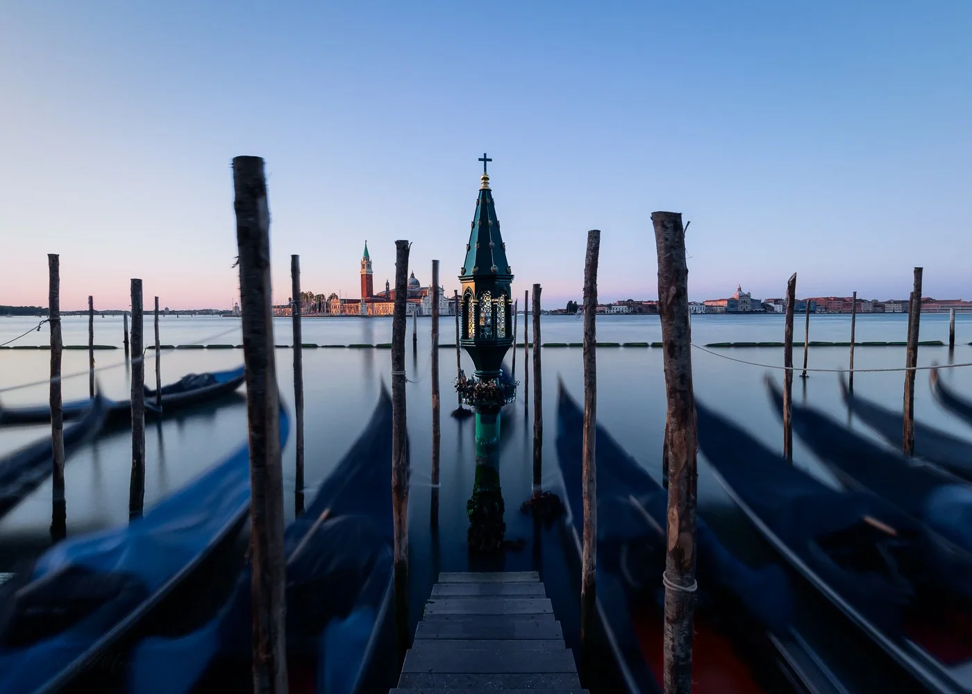 Long exposure shot at sunrise, with moving gondolas in the foreground and the Island of San Giorgio Maggiore in the background, capturing the motion and calm of Venice’s canals.
