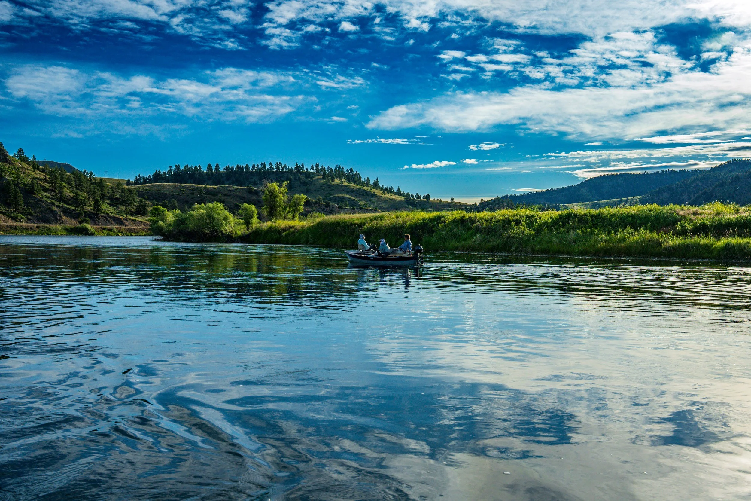 Drift boat far downriver under blue sky, Montana